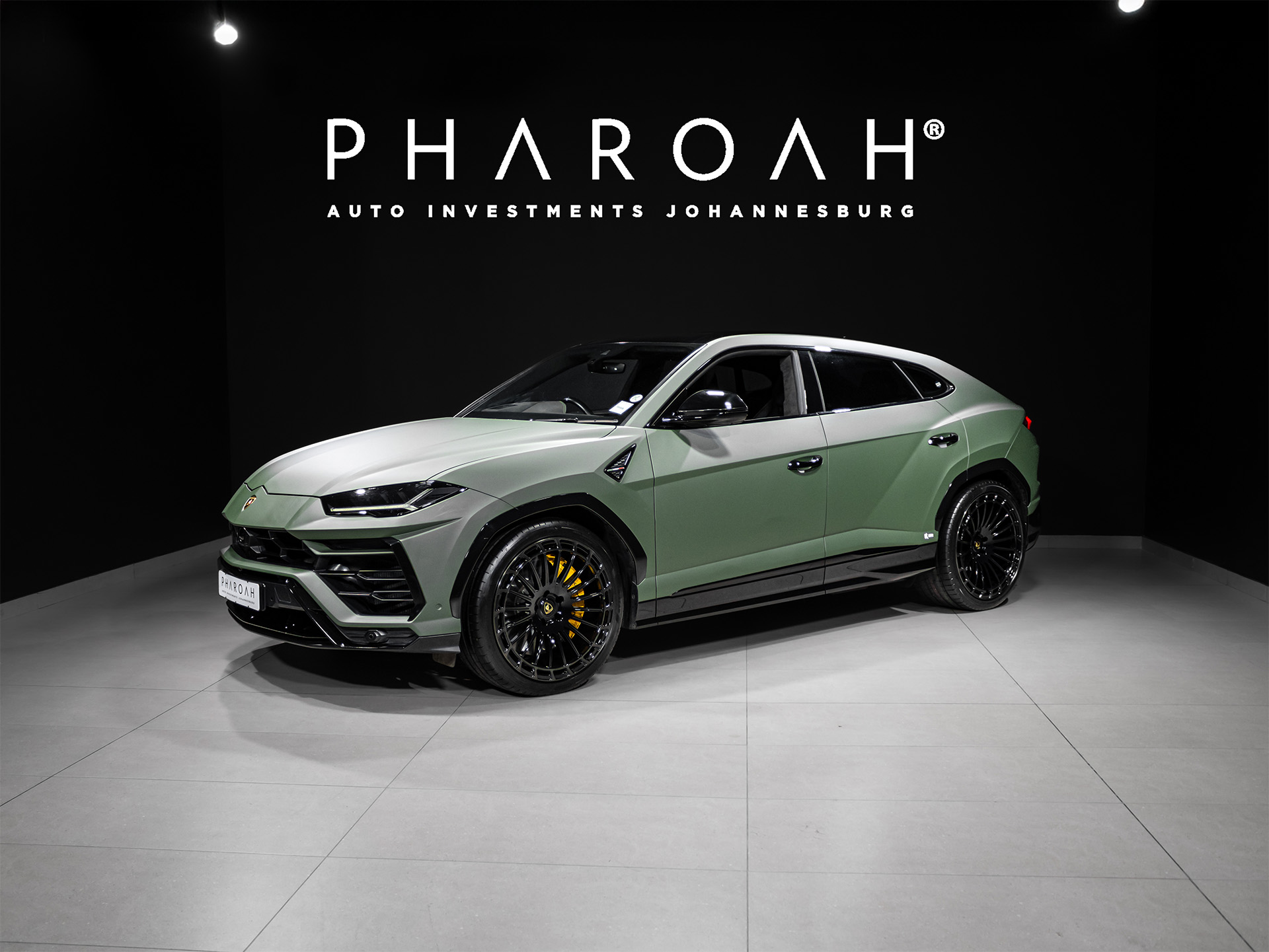 Front three-quarter view of a lime-green Lamborghini SUV on display in a showroom with a black wall and Pharaoh Auto Investme