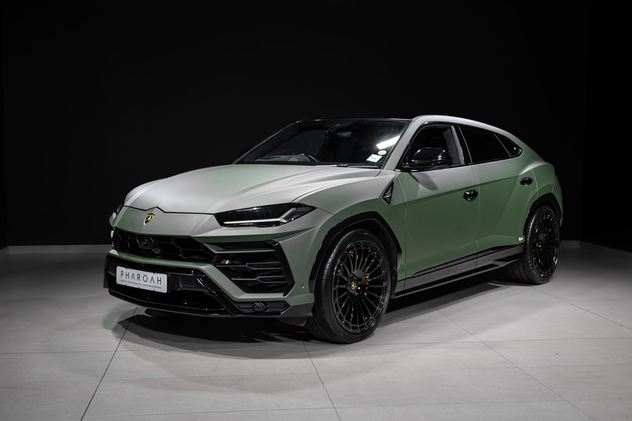 Three-quarter front view of a green Lamborghini SUV with black alloy wheels in a dark studio setting