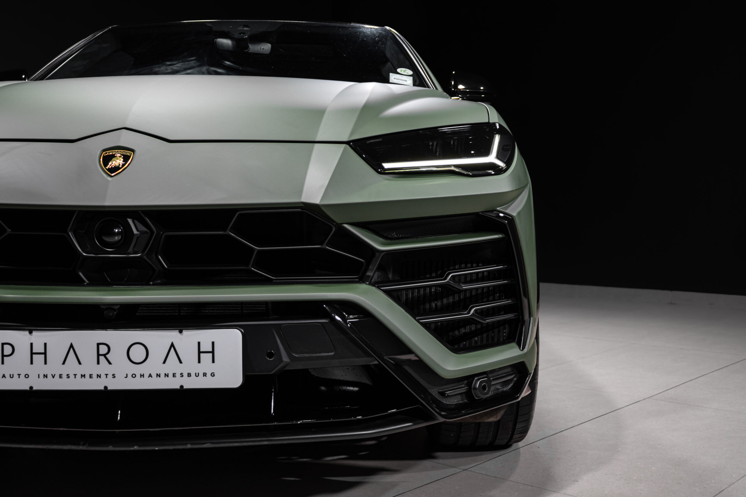 Front close-up of a light green Lamborghini with angular LED headlight and hexagonal grille, license plate reading PHAROH Aut