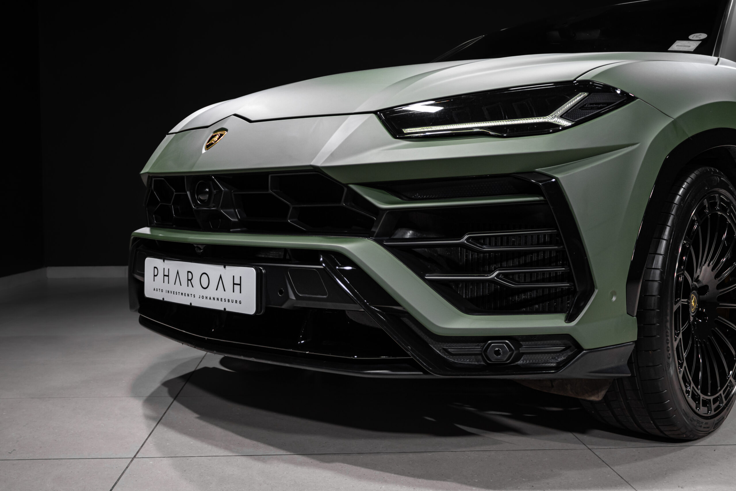 Close-up of a green Lamborghini front end with a sharp LED headlight, hexagonal grille, and the PHAROAH license plate visible