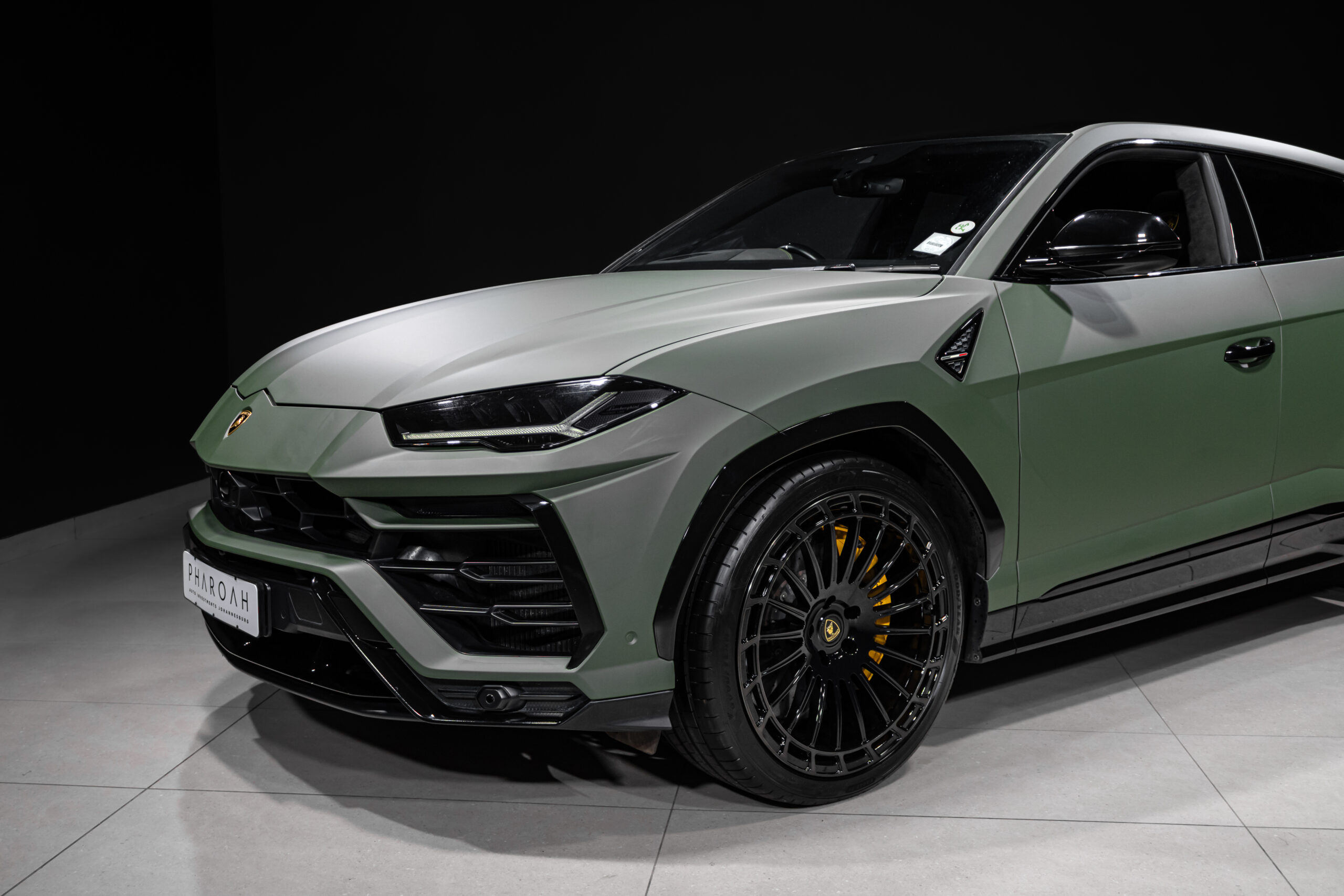 Front-left view of a two-tone green Lamborghini Urus with black roof, showing sculpted hood, headlight, and large alloy wheel