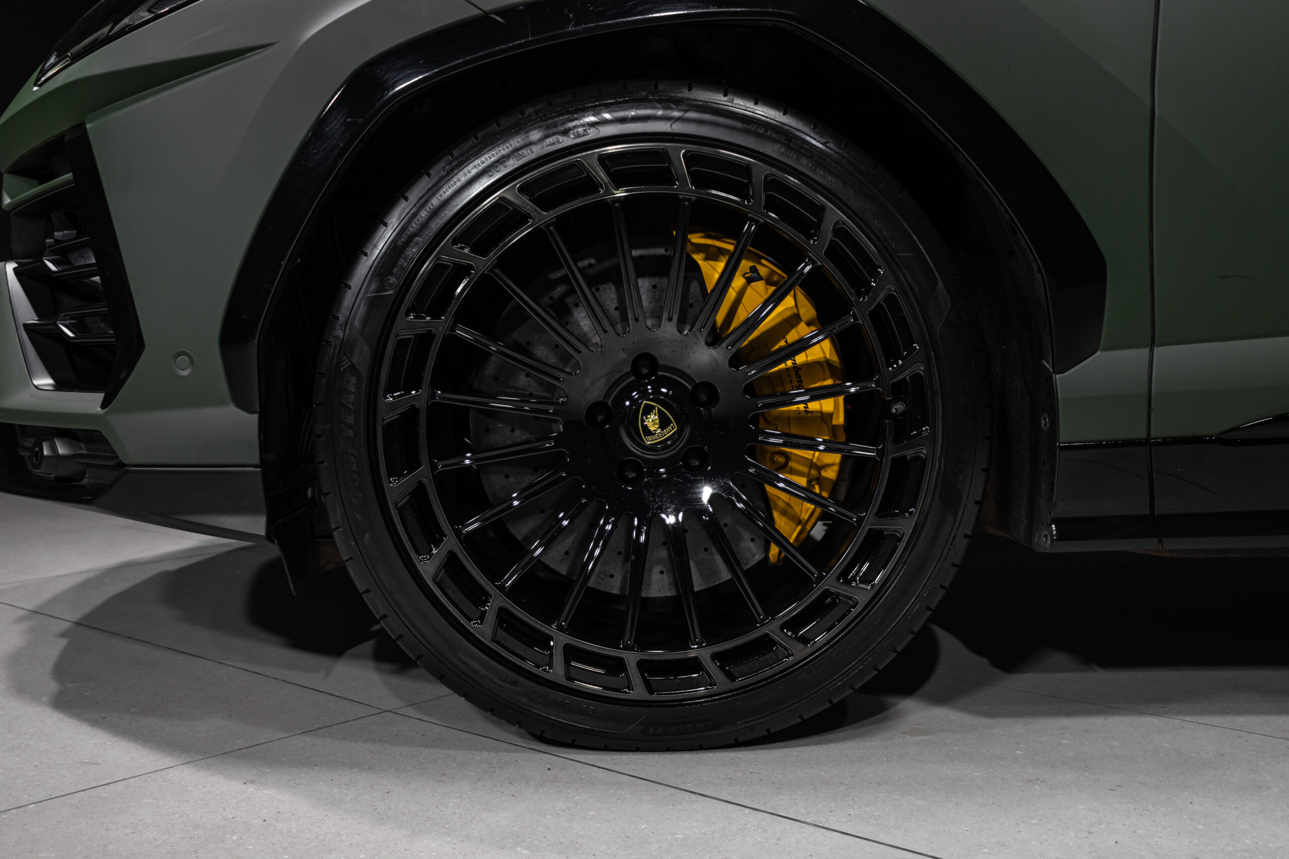 Close-up of a black multi-spoke alloy wheel with a yellow brake caliper visible behind, on a dark green car body.