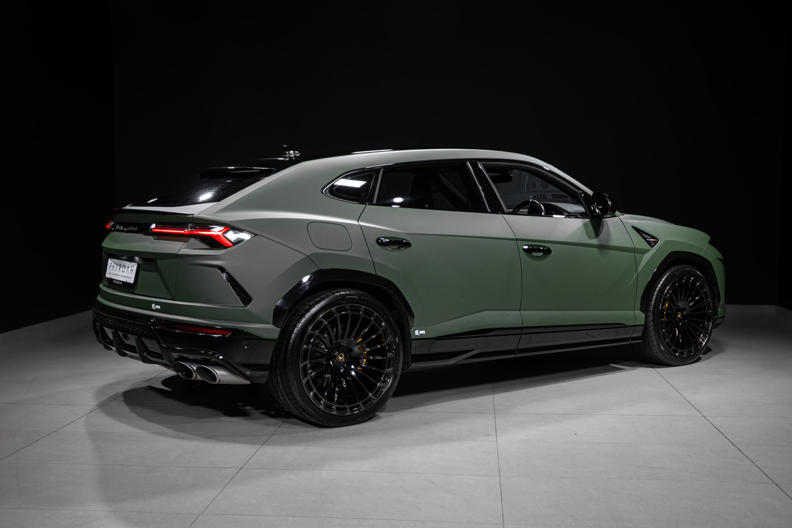 Rear three-quarter view of a lime-green Lamborghini Urus in a dark studio, highlighting large black alloy wheels.