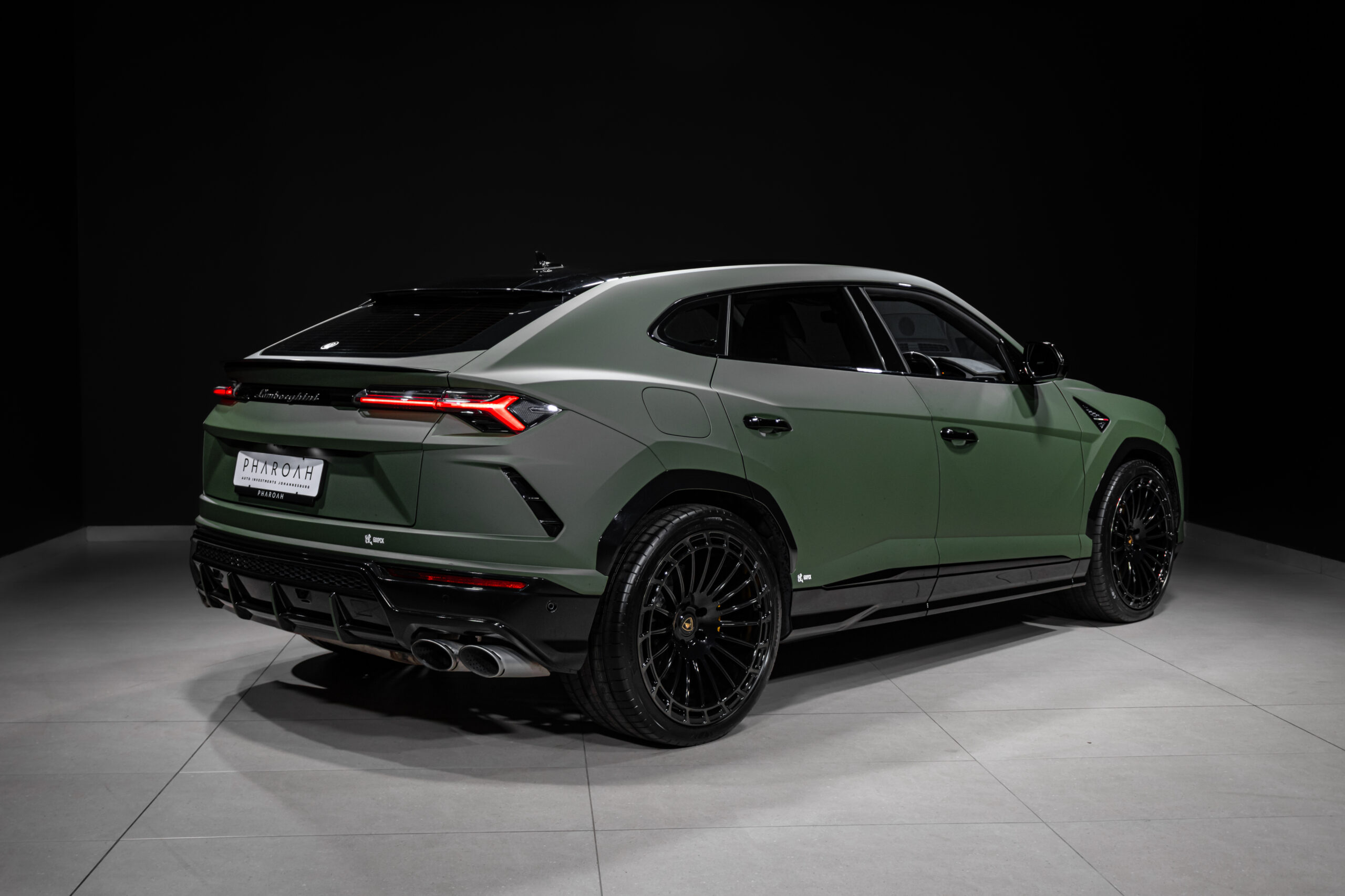 Rear three-quarter view of a green Lamborghini SUV (Urus) in a dark studio, showing the taillights, sculpted rear, and large