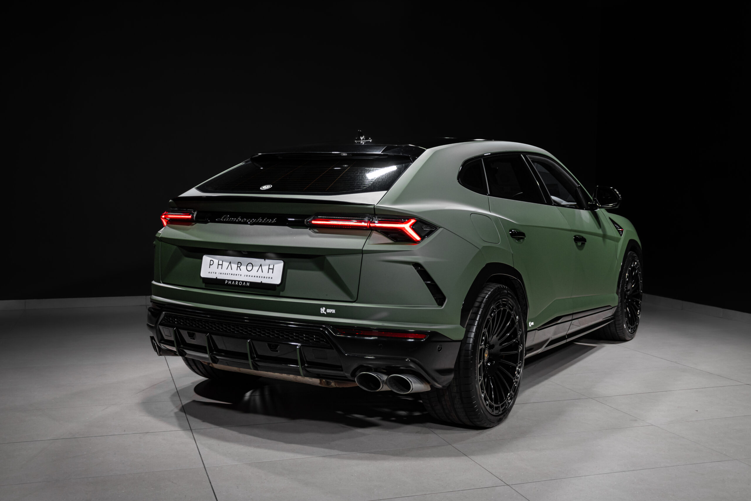 Rear three-quarter view of a green Lamborghini Urus SUV in a dark studio backdrop.