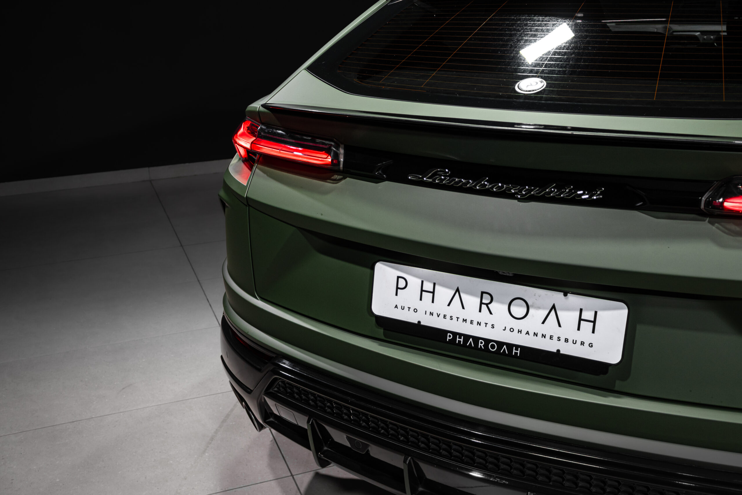 Rear view of a matte green Lamborghini with red taillights, chrome badging, and a customized 'PHAROAH' license plate visible