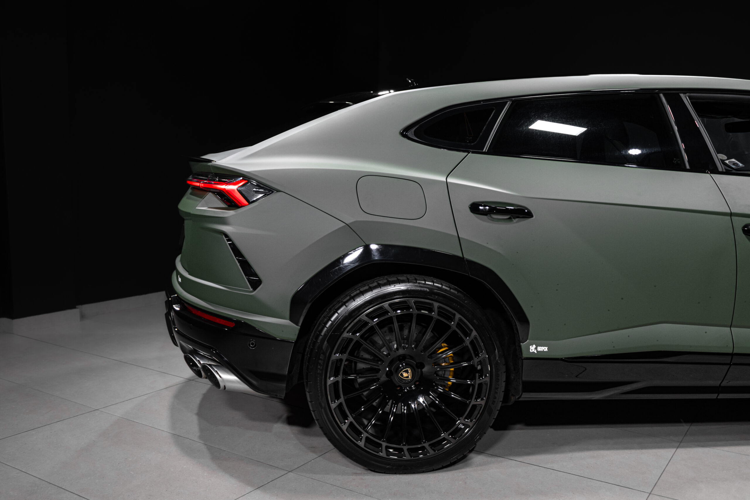 Green luxury SUV shown from the rear-left side in a dark studio, featuring a red taillight and large black multi-spoke wheel.