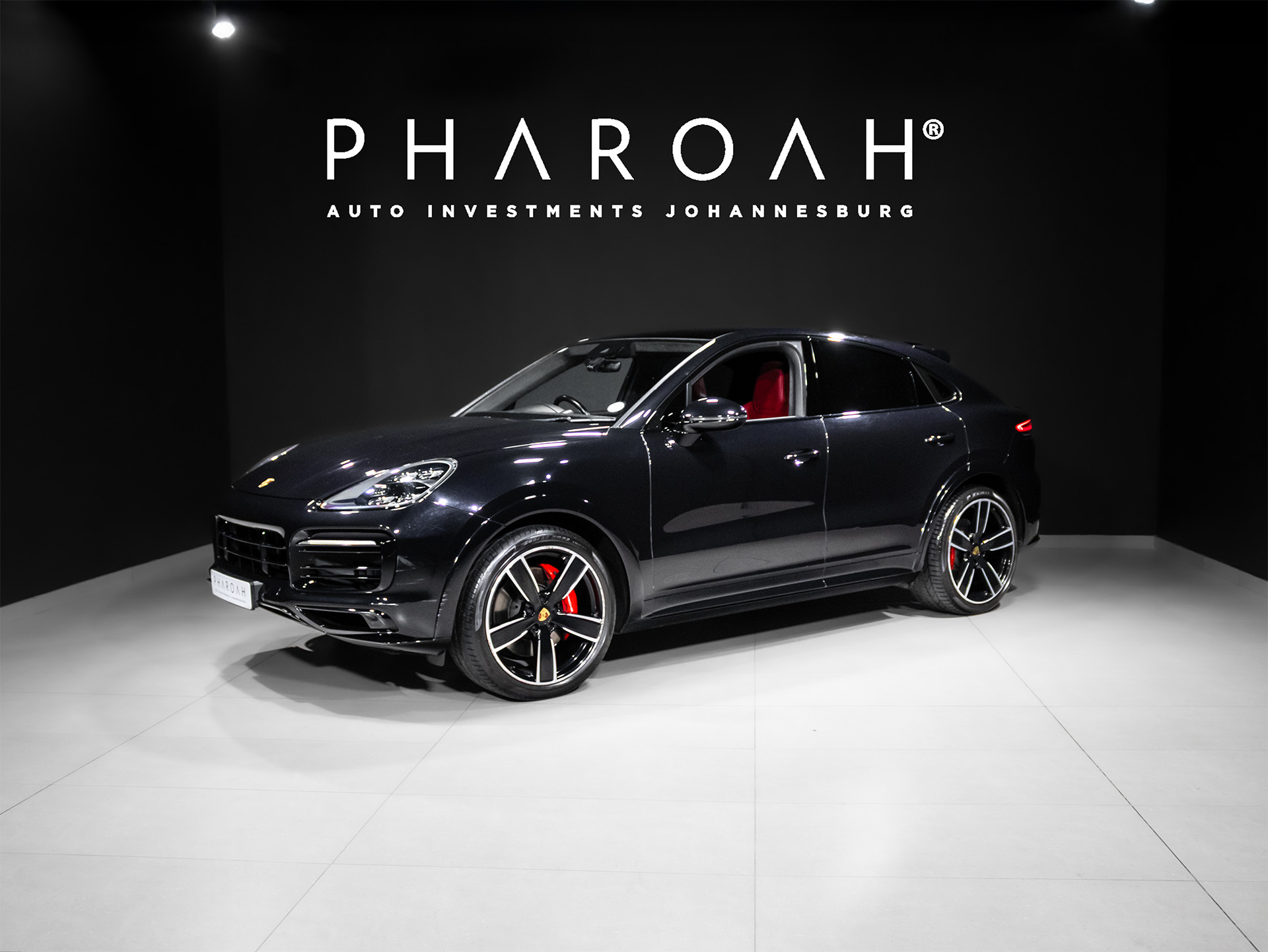 Dark blue Porsche SUV on a clean showroom floor, red interior visible through the windows, with PHAROAH Auto Investments Joha