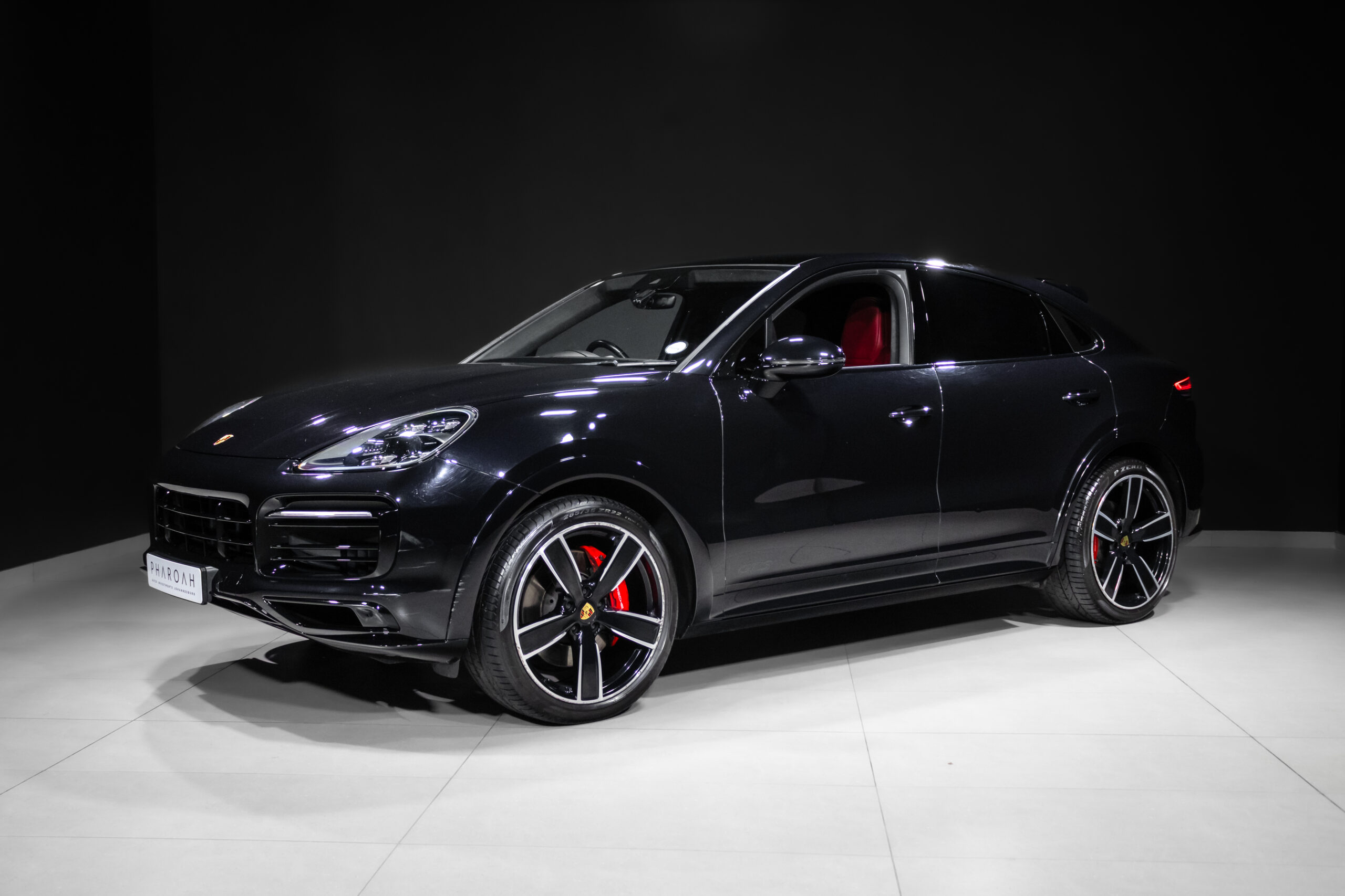 Black Porsche SUV in a studio setting with glossy finish, large alloy wheels, and red brake calipers visible through the whee