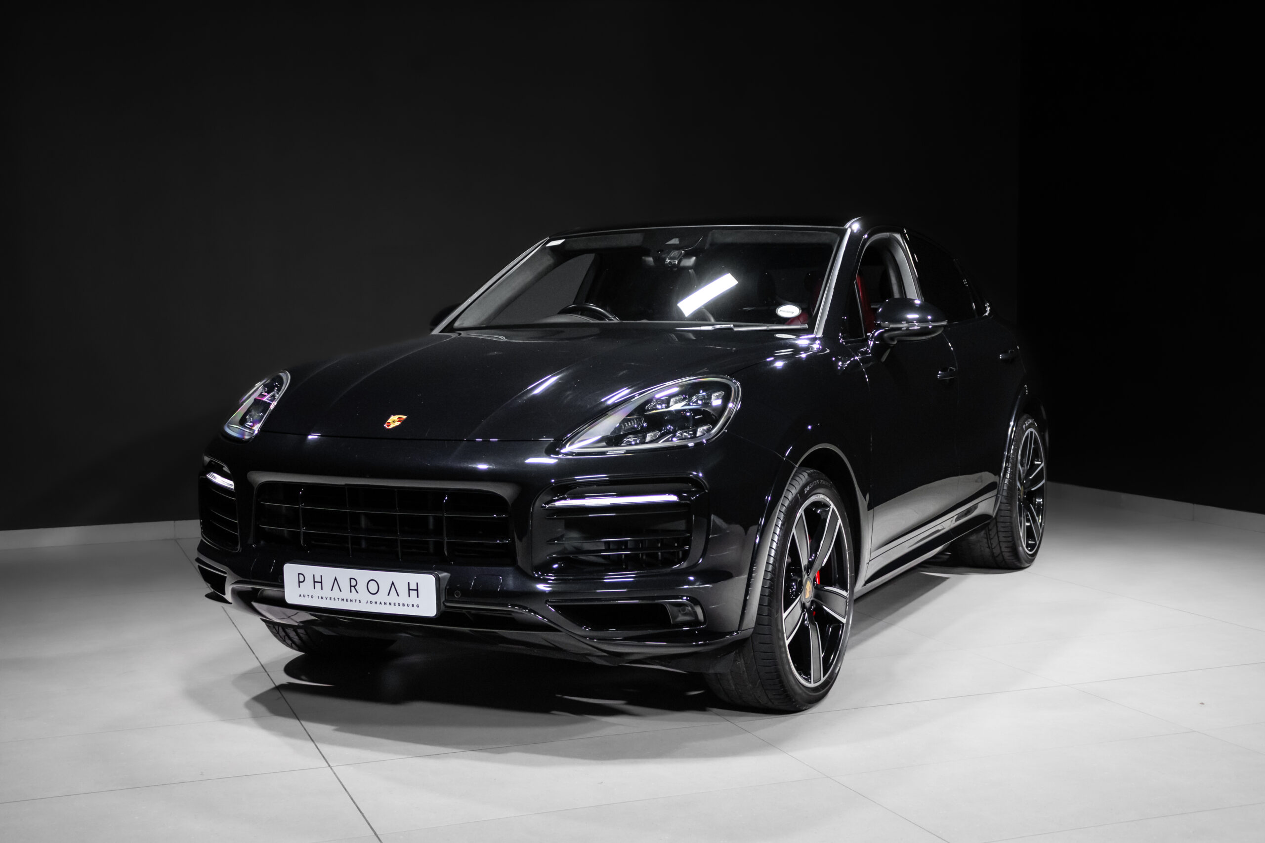 Front-left three-quarter view of a black Porsche SUV in a studio, glossy finish and large alloy wheels on a light showroom fl