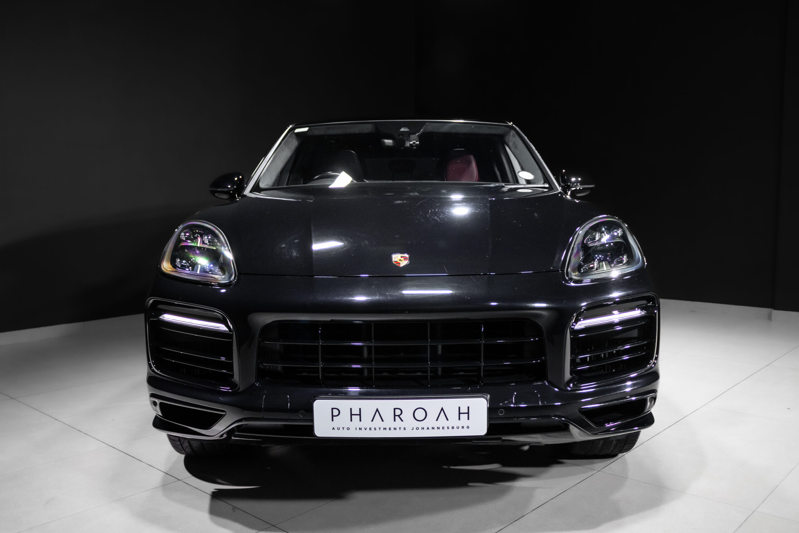 Front view of a dark Porsche SUV in a showroom, license plate reads PHAROAH Auto Investments Johannesburg.