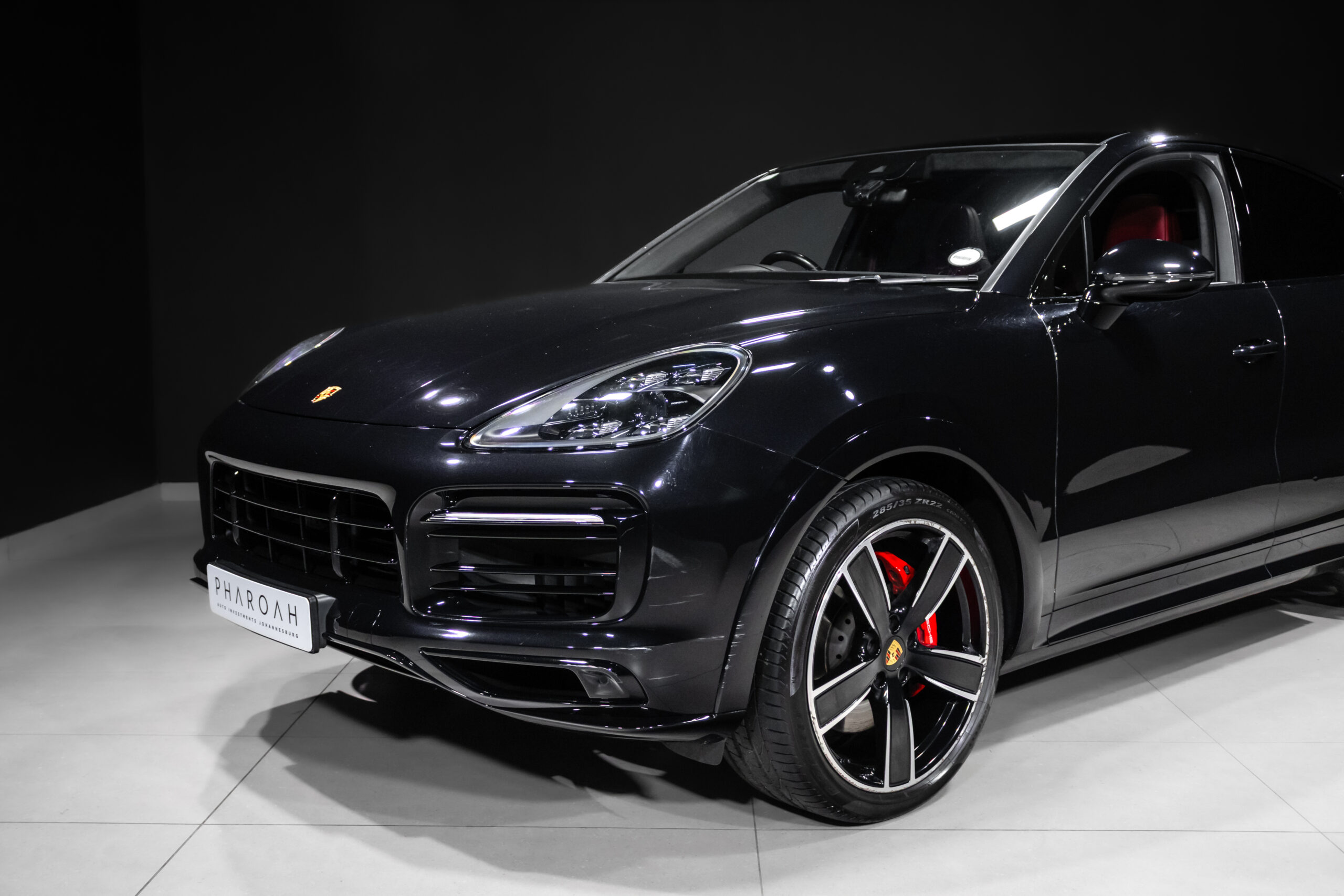 Black Porsche SUV in a showroom, front three-quarter view, glossy finish and red brake calipers visible behind large alloy wh