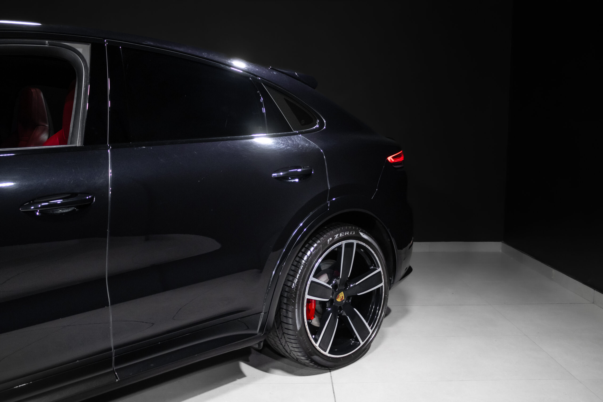 Close-up of the rear side of a black SUV in a studio, highlighting large alloy wheels with a Porsche crest and red brake cali