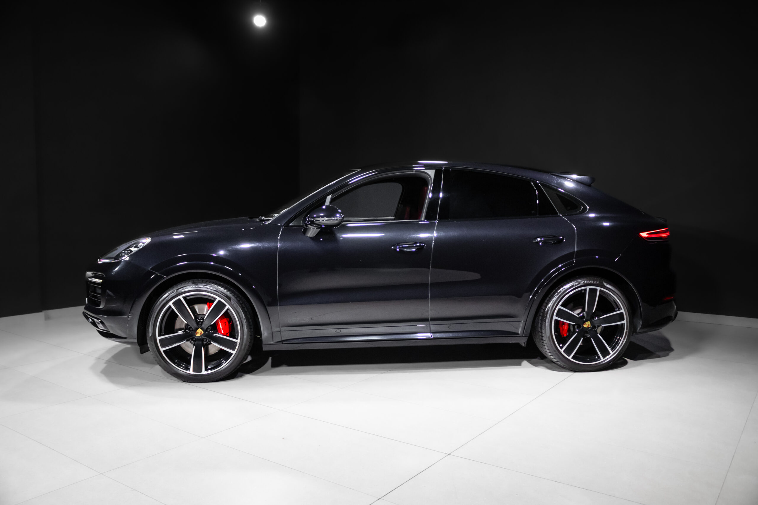 Side view of a dark blue Porsche SUV on a white showroom floor, with red brake calipers visible under glossy wheels.