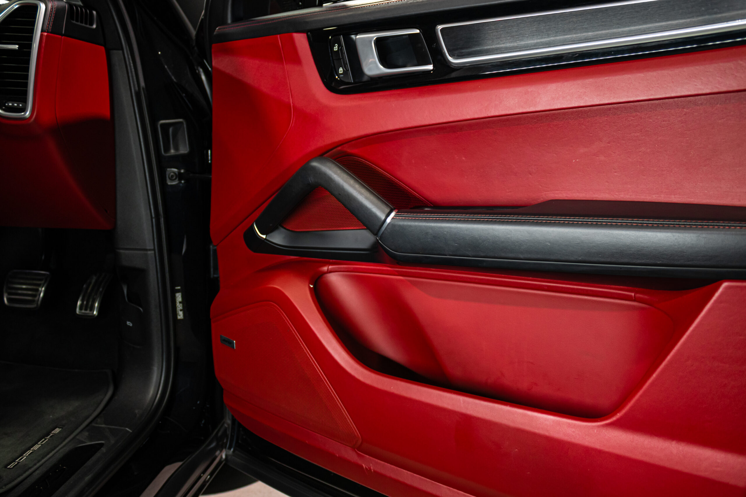 Red interior car door with black armrest, silver door handle, and speaker panel.
