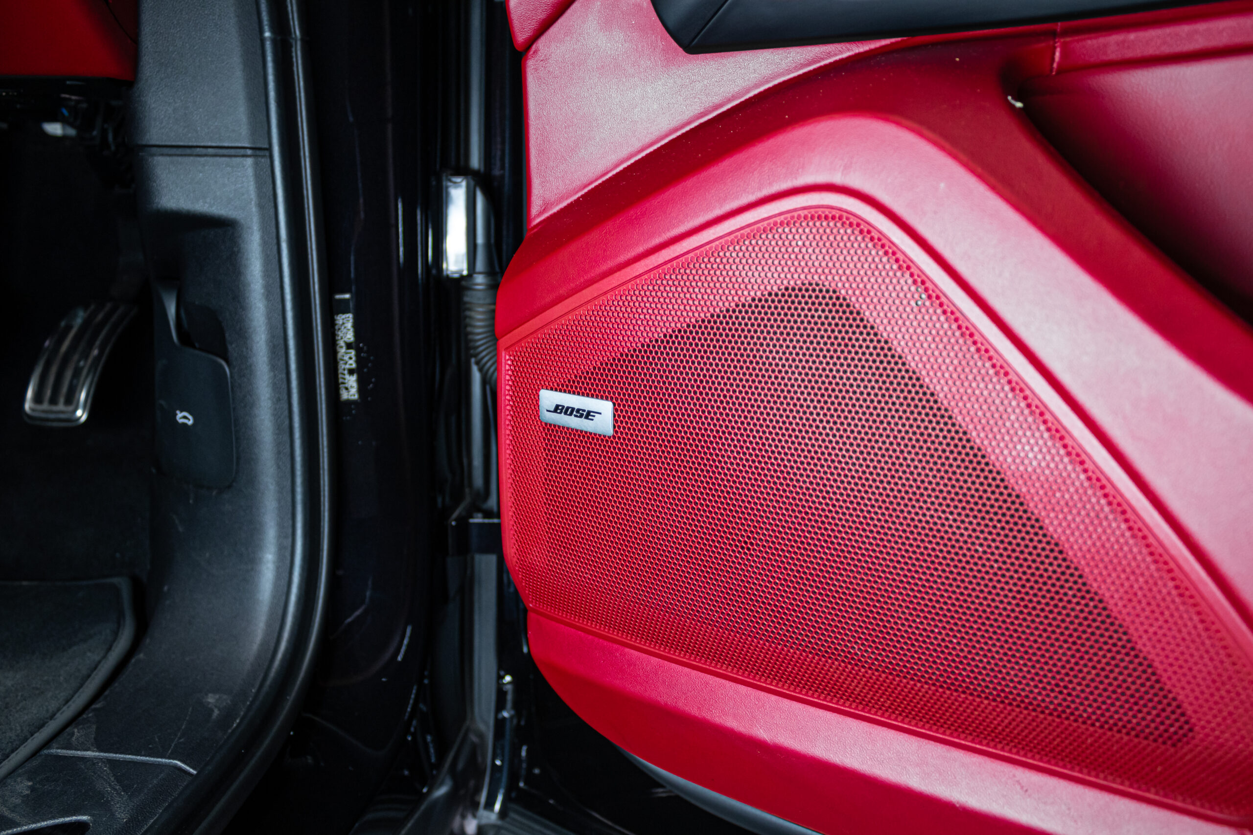 Red car door interior focusing on the perforated speaker grille with a Bose badge nearby.