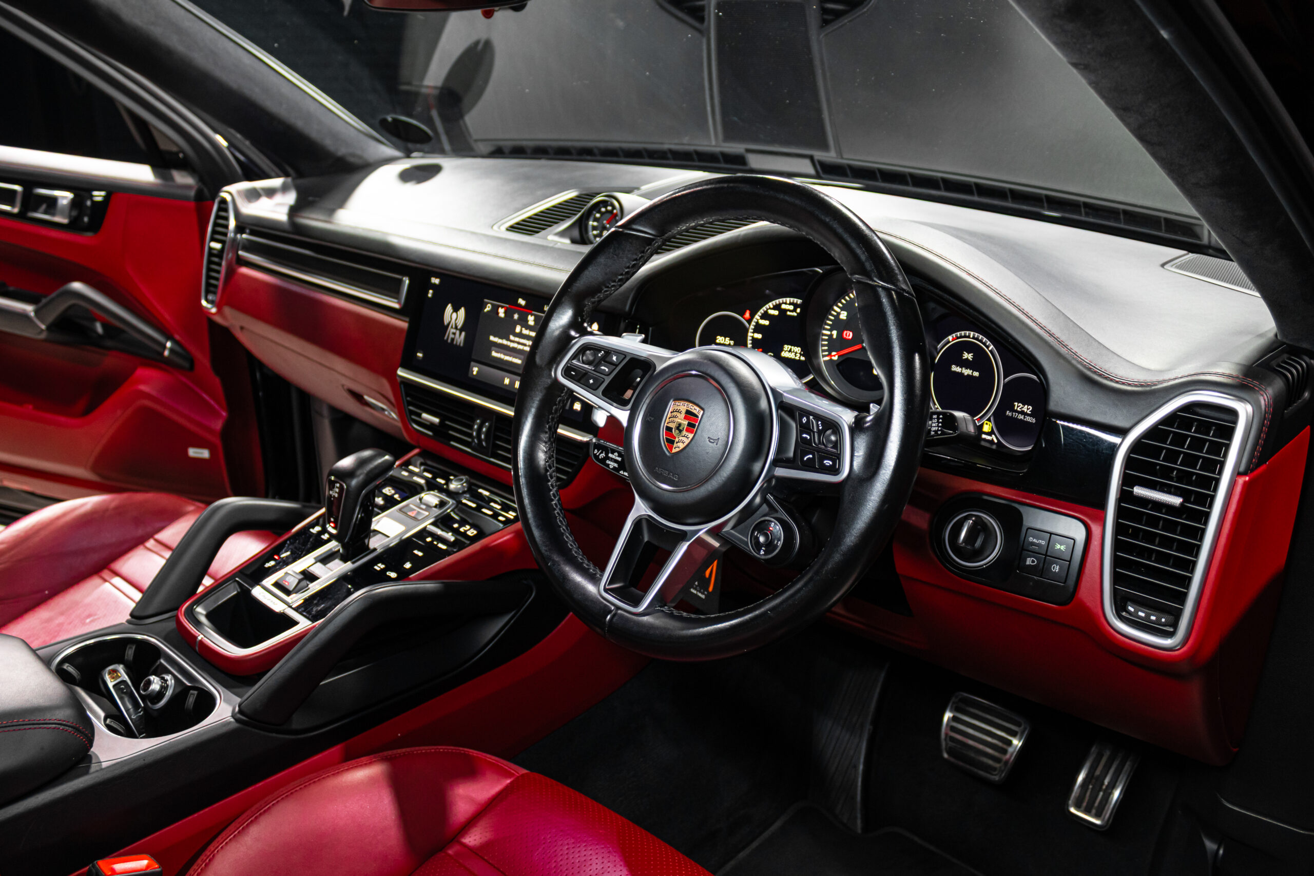 Red leather-car interior featuring a Porsche steering wheel and high-tech center console with digital gauges.