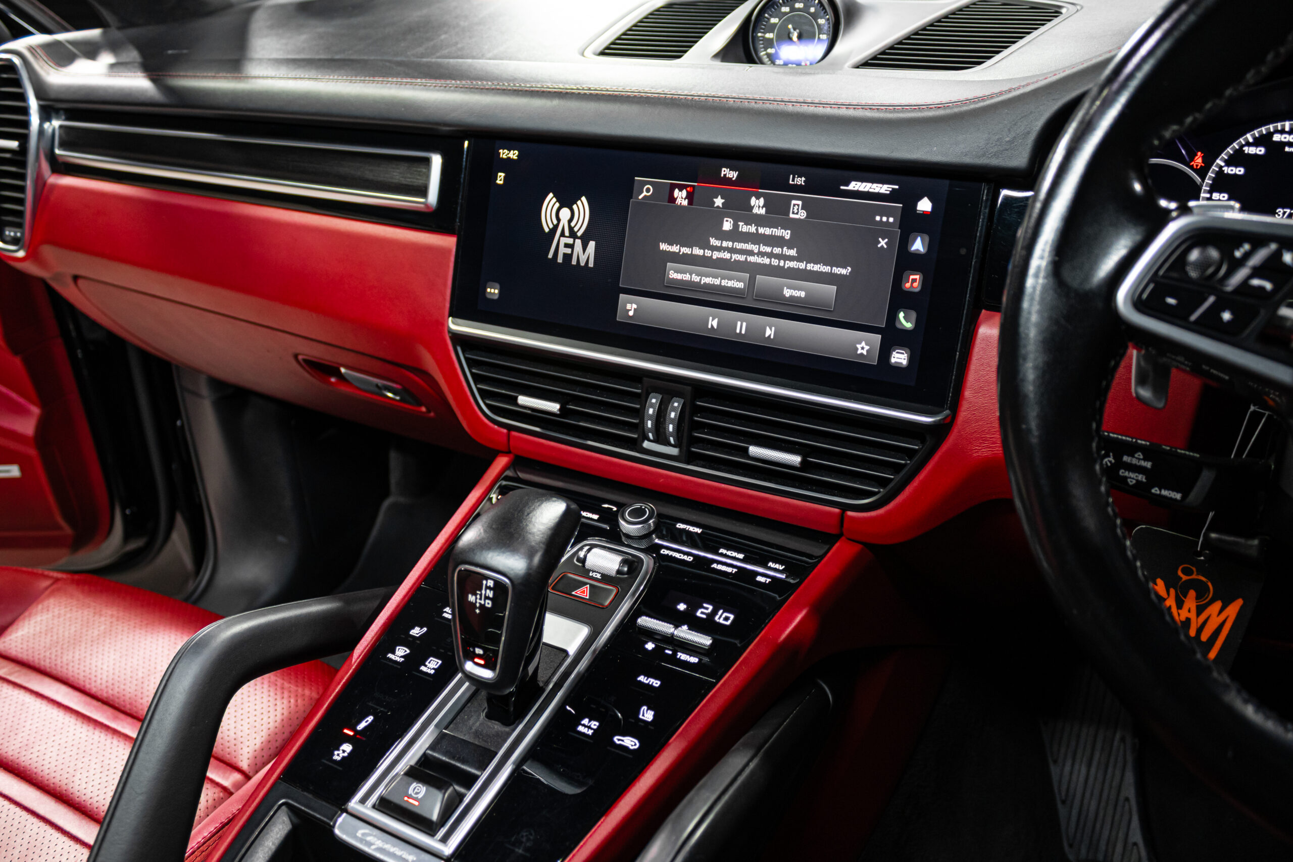 Red-leather car cabin with a wide center touchscreen displaying FM radio and media controls