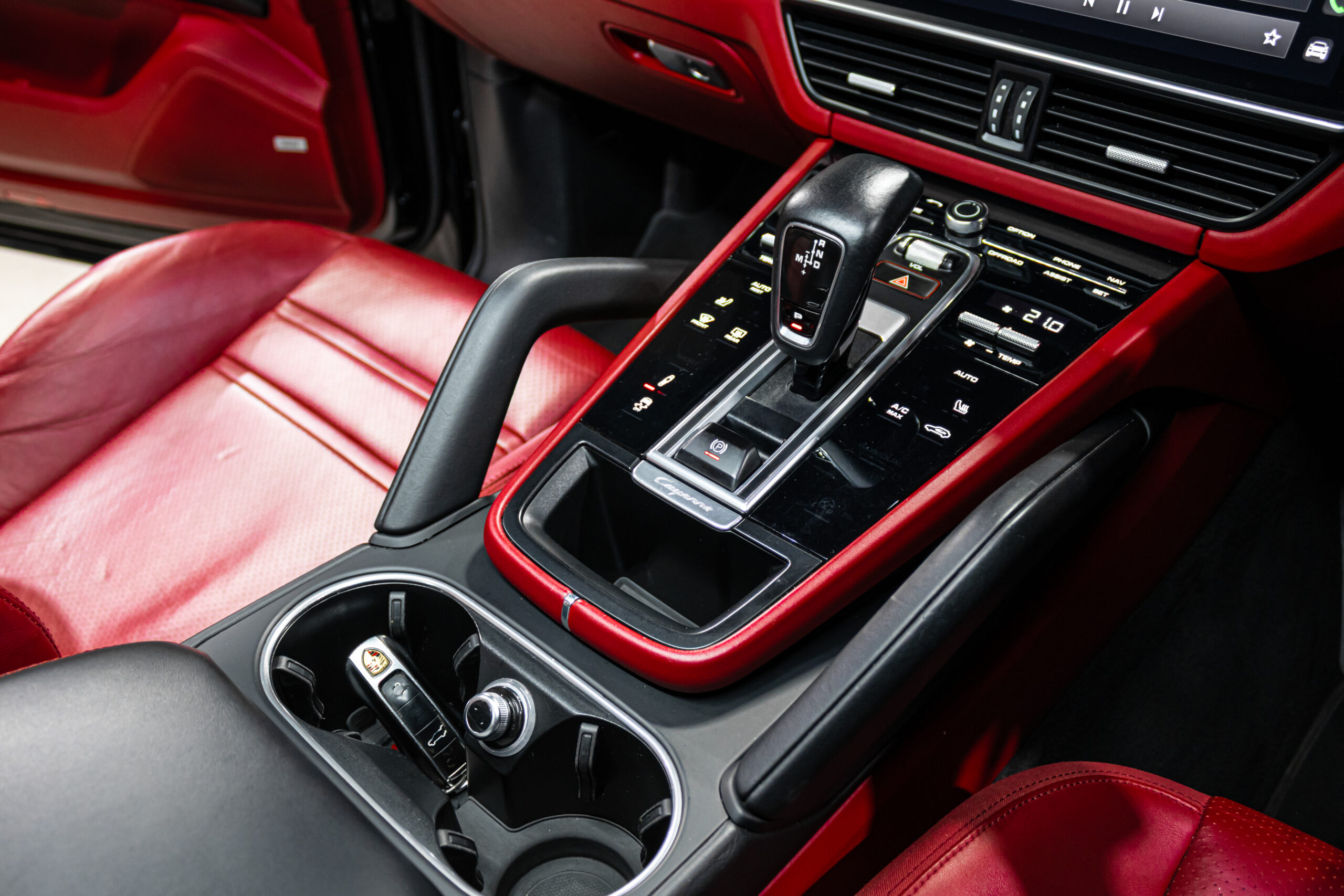 Red leather car interior focusing on the center console with a black gear selector and surrounding controls; Porsche key fob