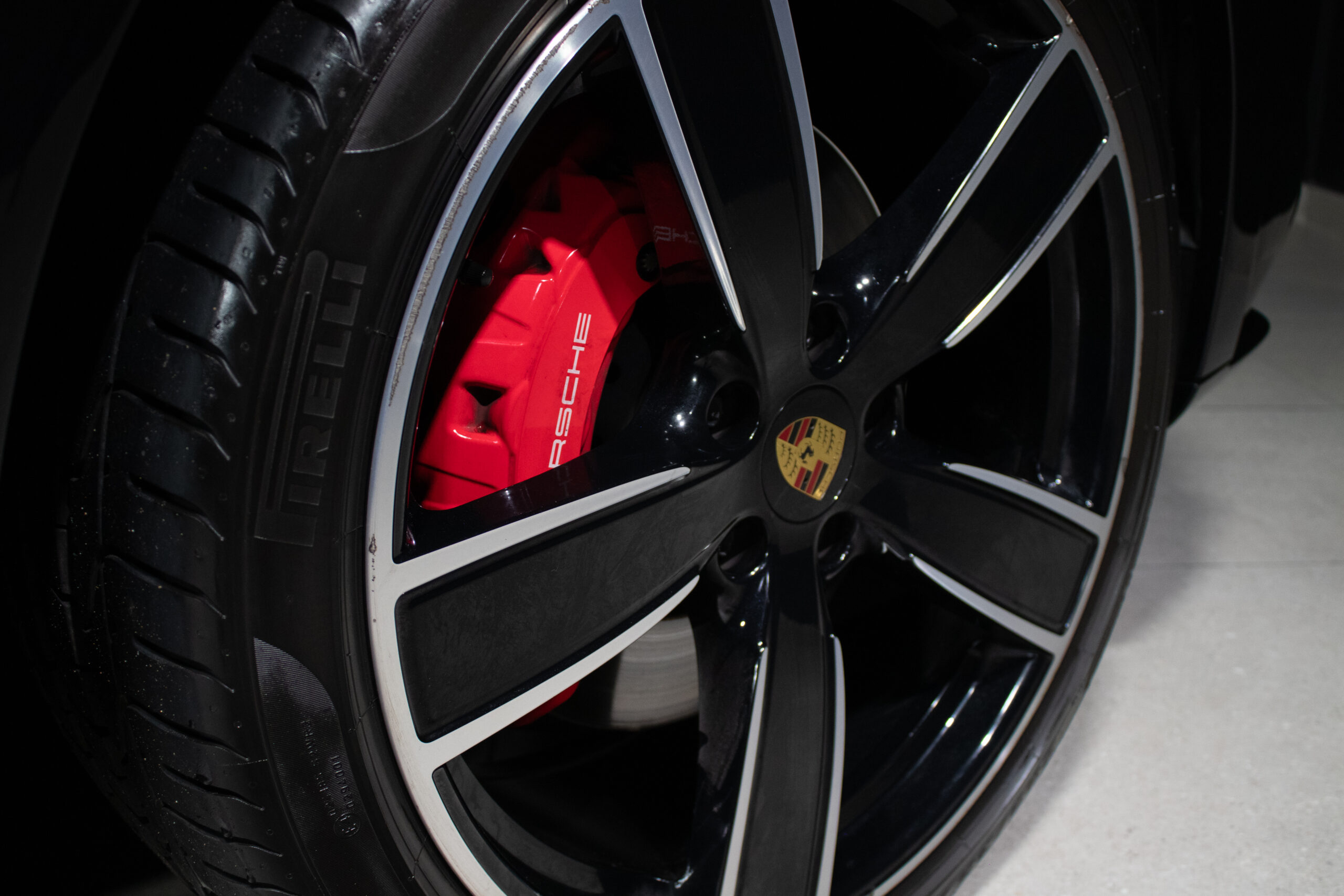 Close-up of a Porsche wheel showing a red brake caliper with Porsche lettering behind a black and silver alloy rim with the c
