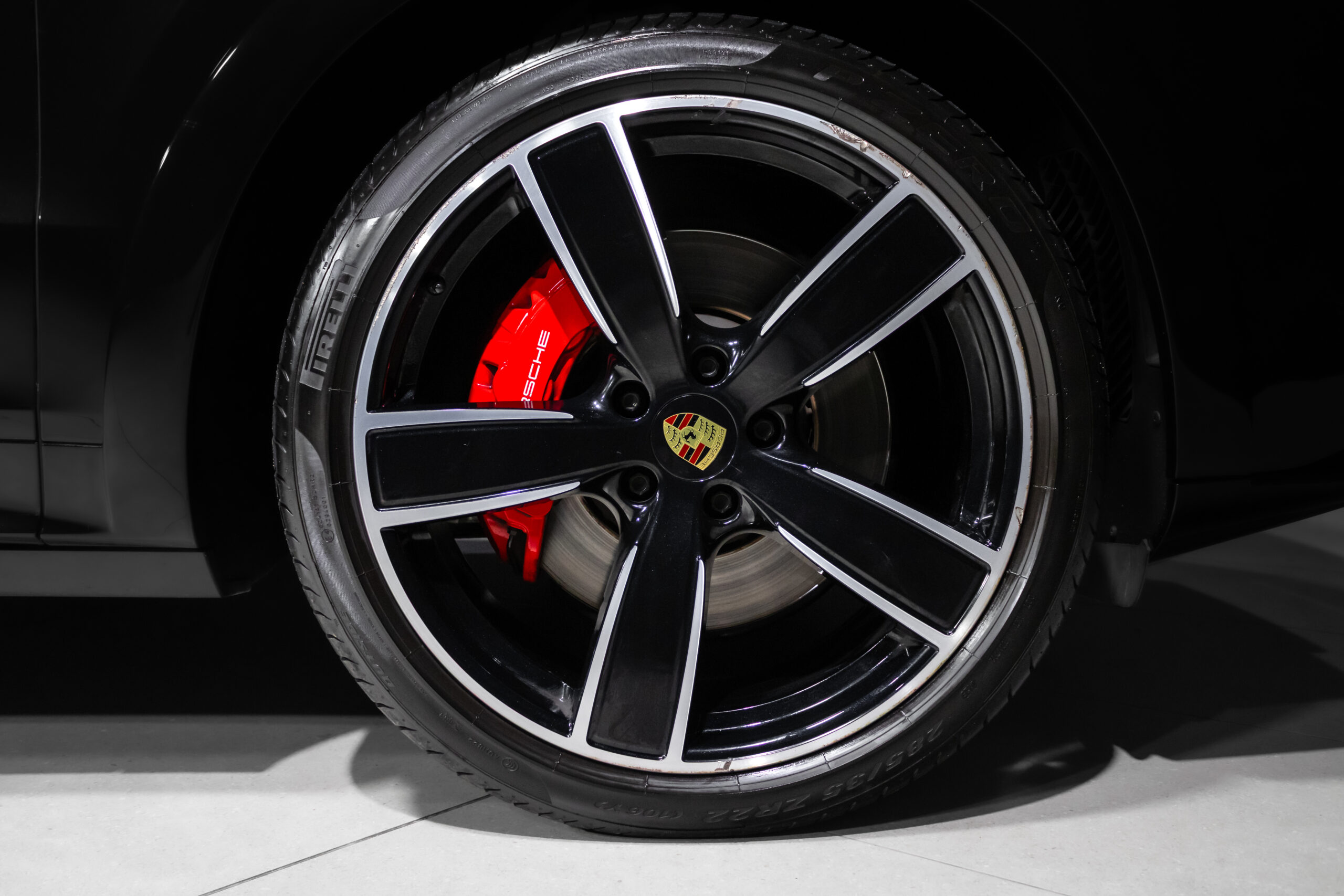 Close-up of a black alloy wheel with five double spokes, red brake caliper, and Porsche crest center cap.