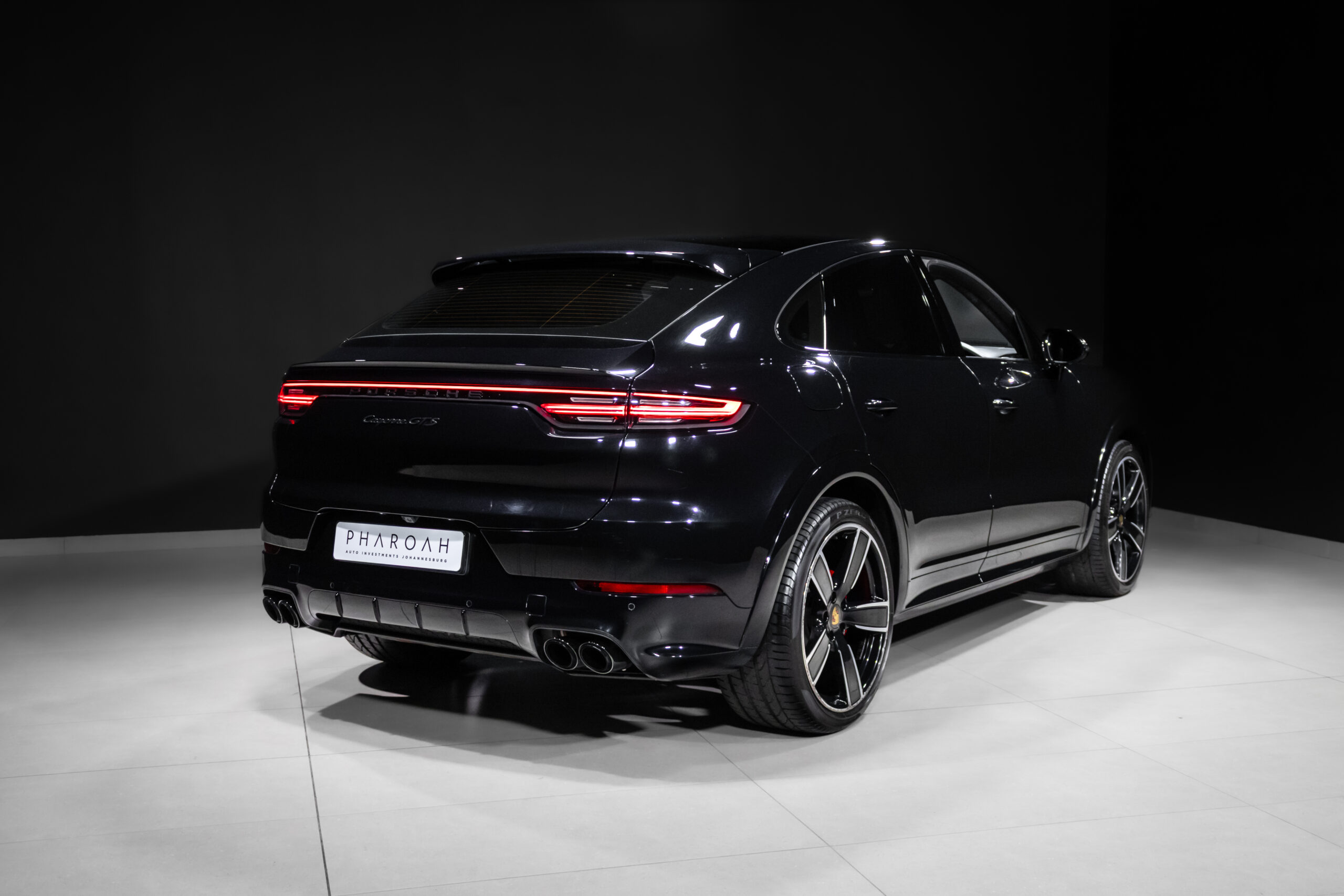 Black Porsche SUV (Cayenne GTS) shown from rear three-quarter view in a clean showroom with glossy floor and dramatic lightin