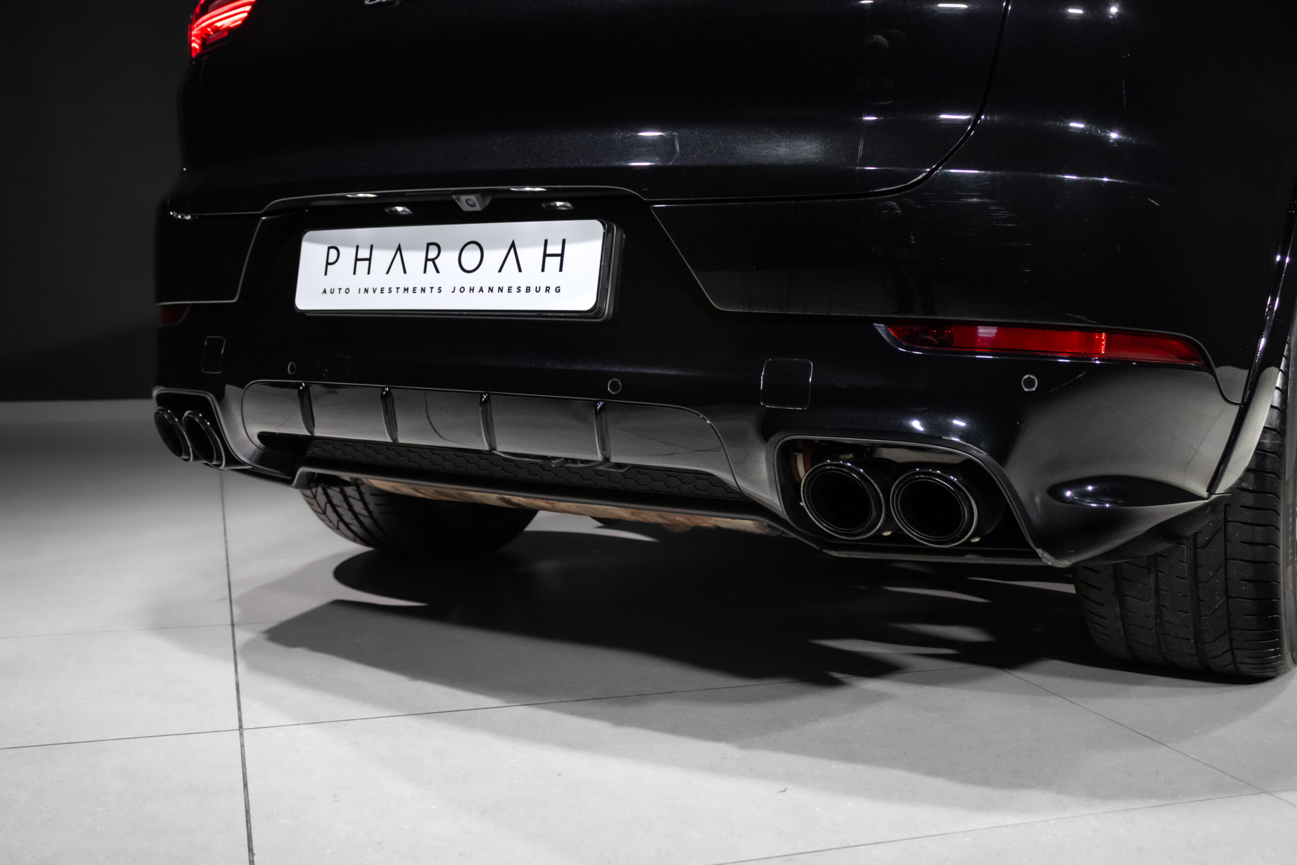 Rear view of a black SUV showing quad exhaust pipes and a white license plate on a showroom floor.