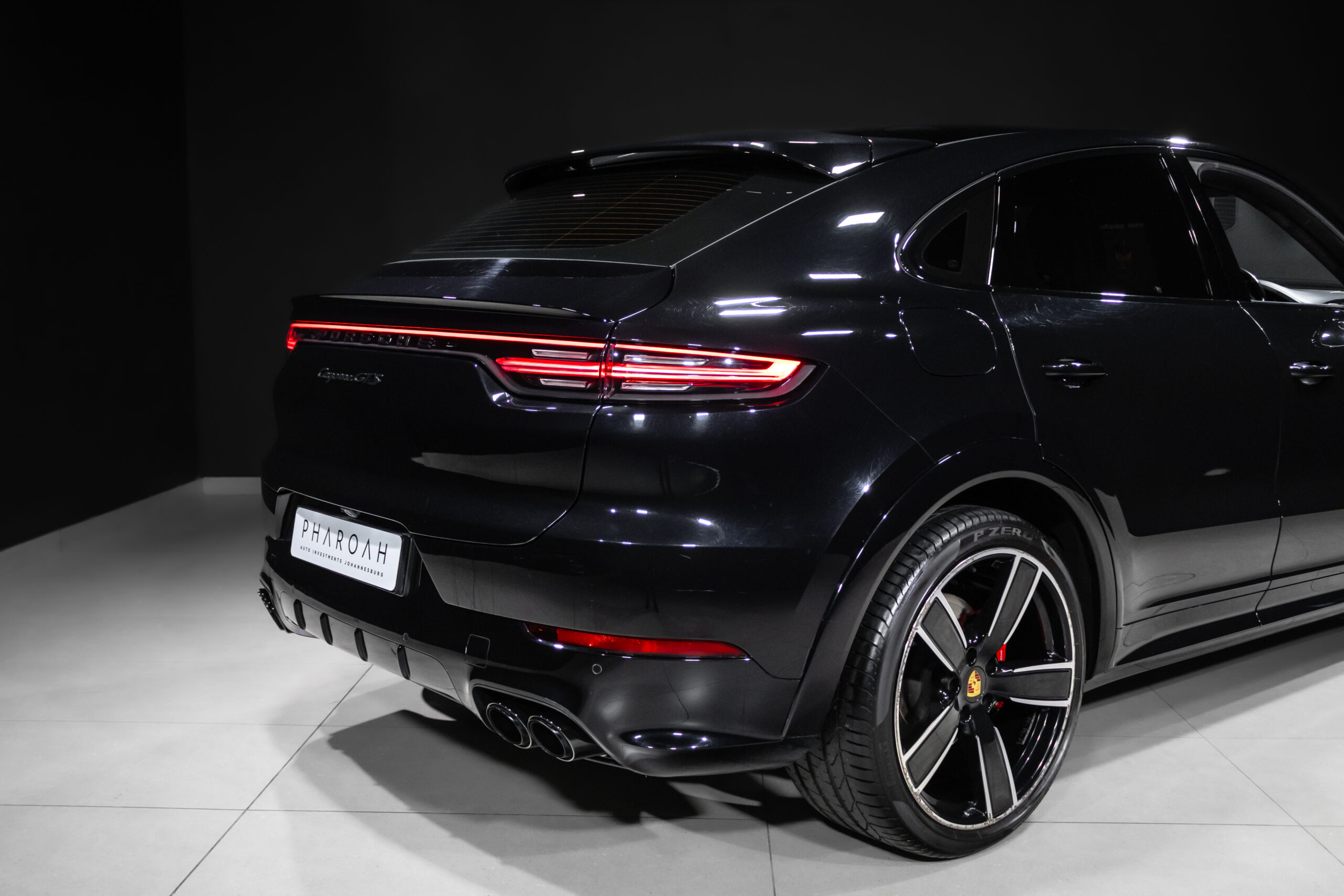 Rear three-quarter view of a glossy black luxury SUV with red LED taillights and quad exhausts in a showroom setting.
