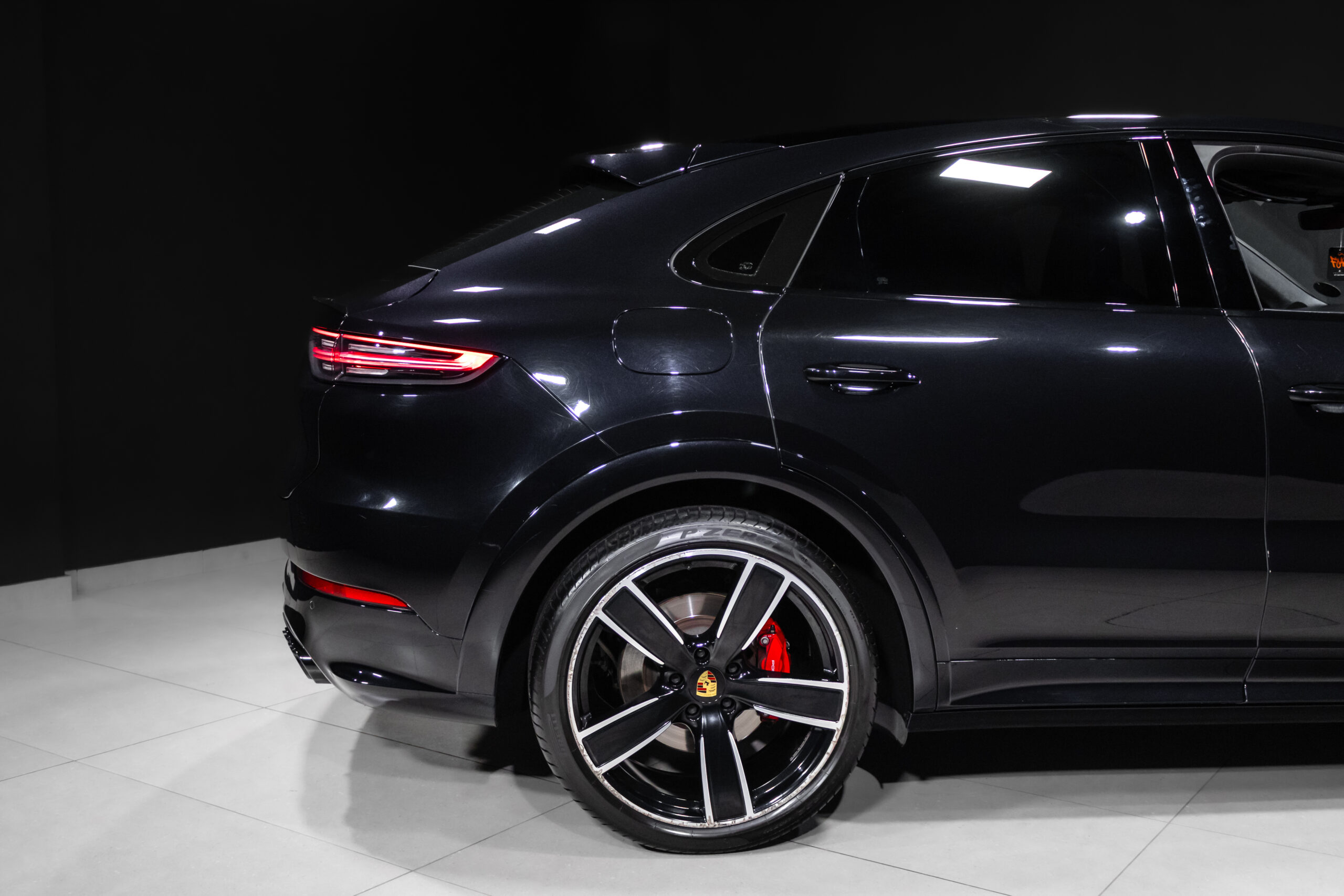 Rear quarter view of a black Porsche SUV in a showroom, with red brake calipers visible through large alloy wheels.
