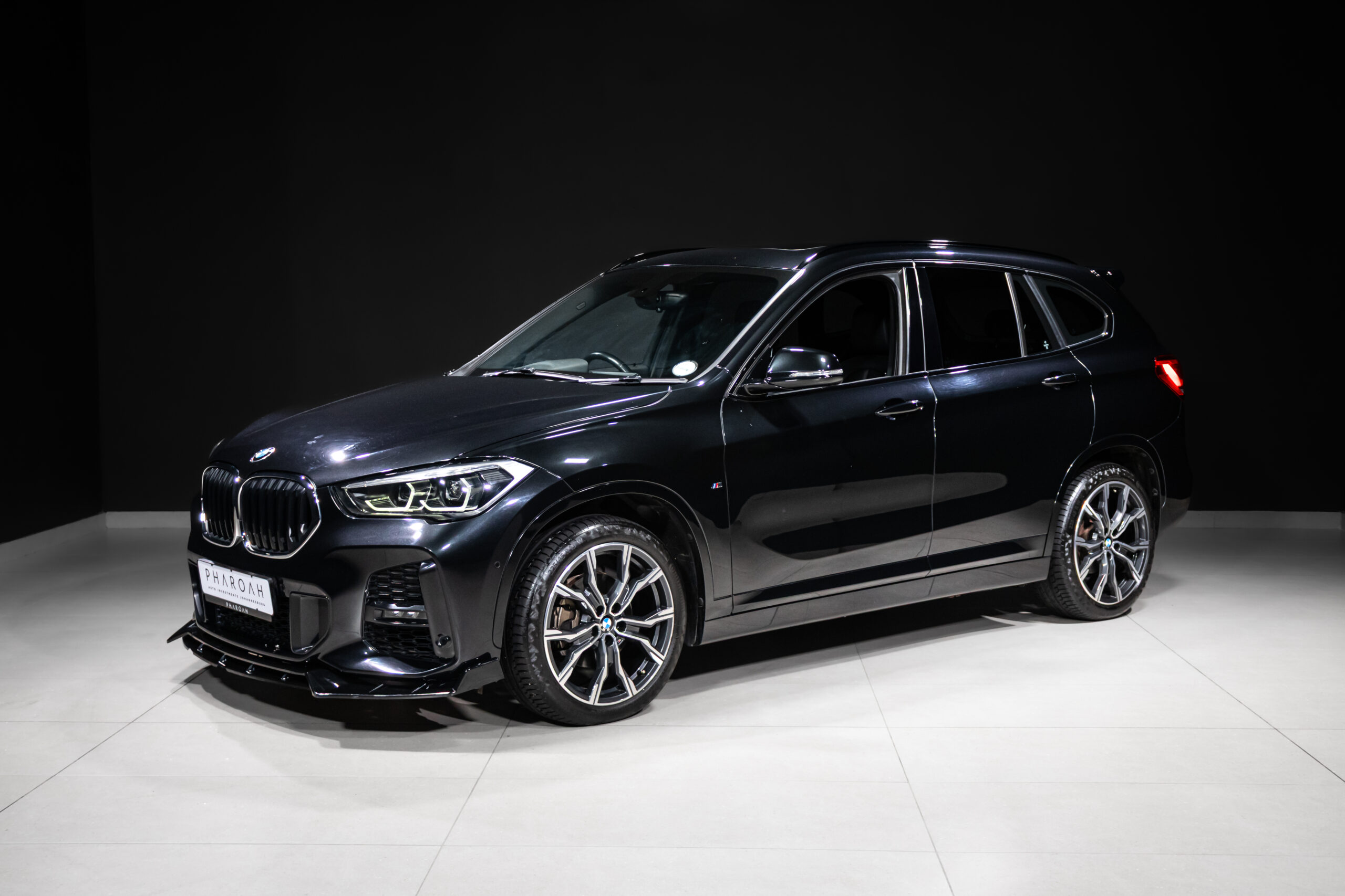 Black BMW SUV on a showroom floor, angled to the front-left with chrome wheels visible