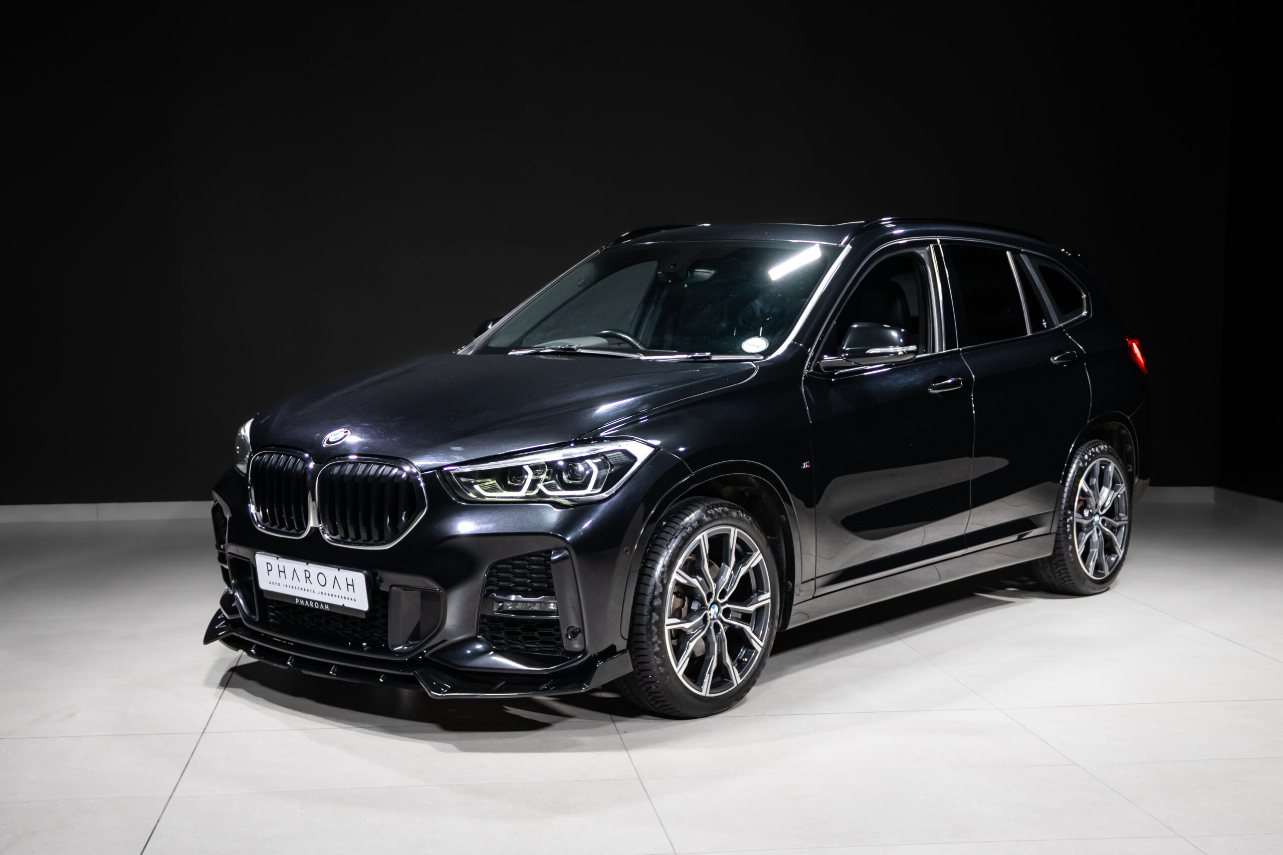 Black BMW SUV in a studio showroom, three-quarter front view with chrome kidney grille and LED headlights.