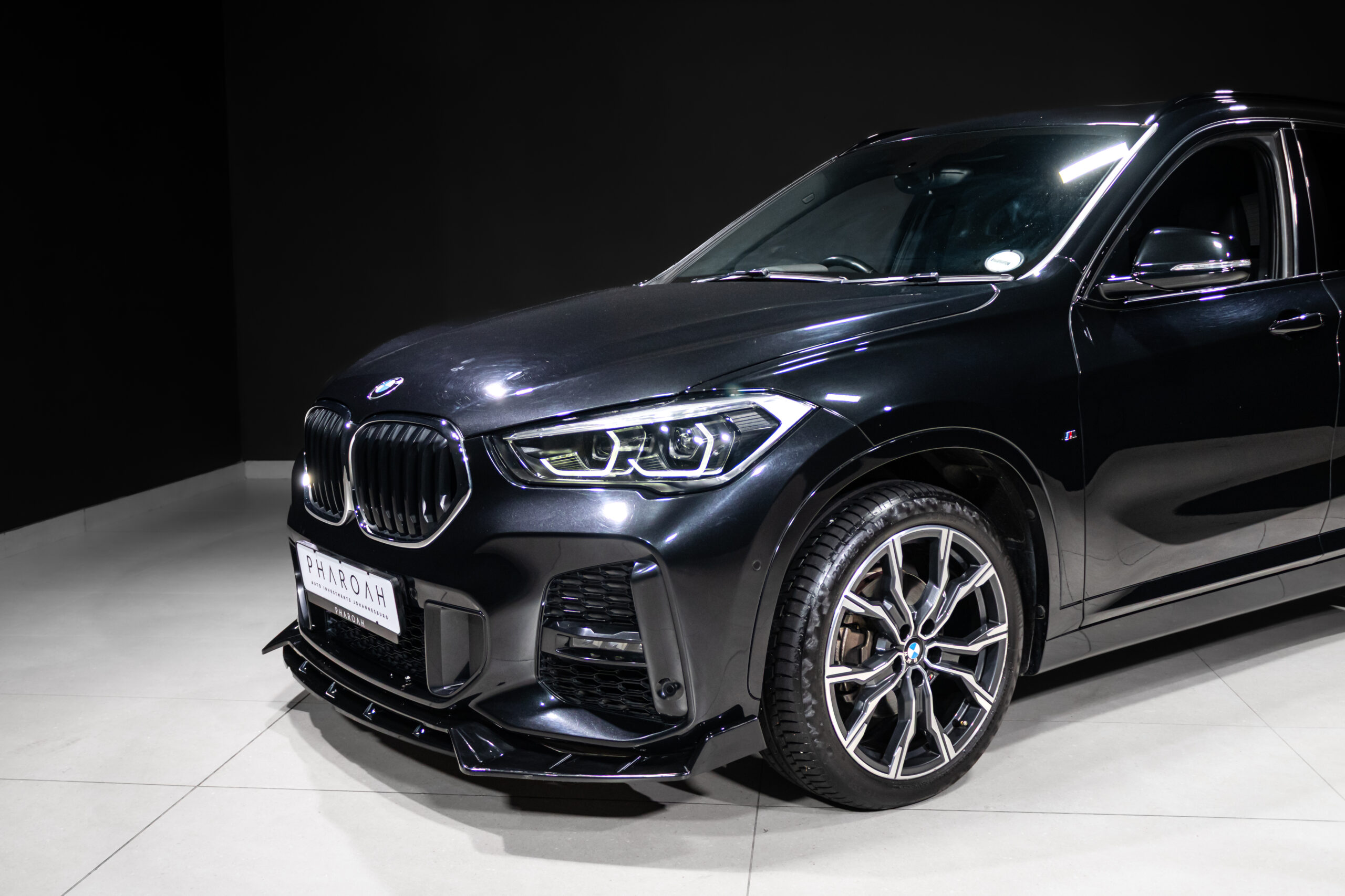 Black BMW SUV shown in a showroom, angled to reveal the front grille, LED headlights, and large alloy wheels.