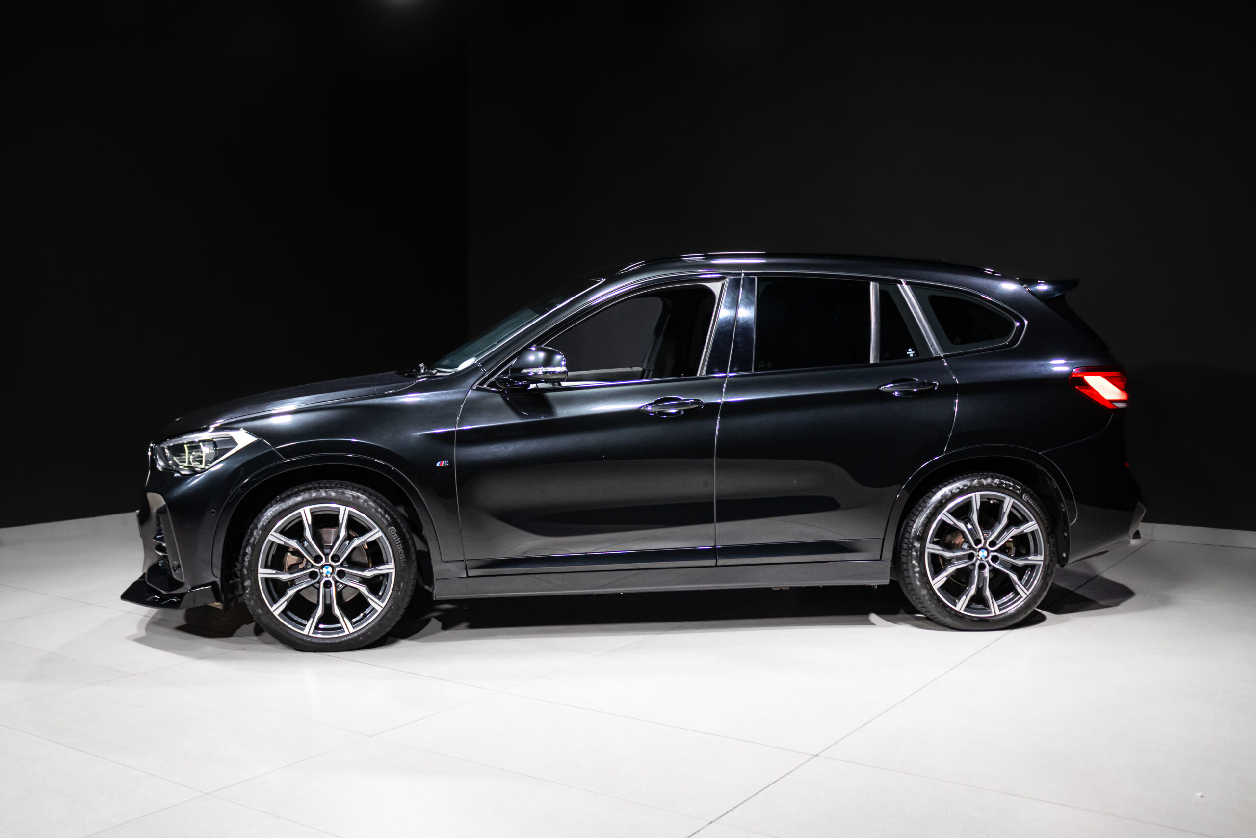 Side view of a black BMW SUV in a studio, showing glossy paint, chrome mirrors, and large multi‑spoke alloy wheels.