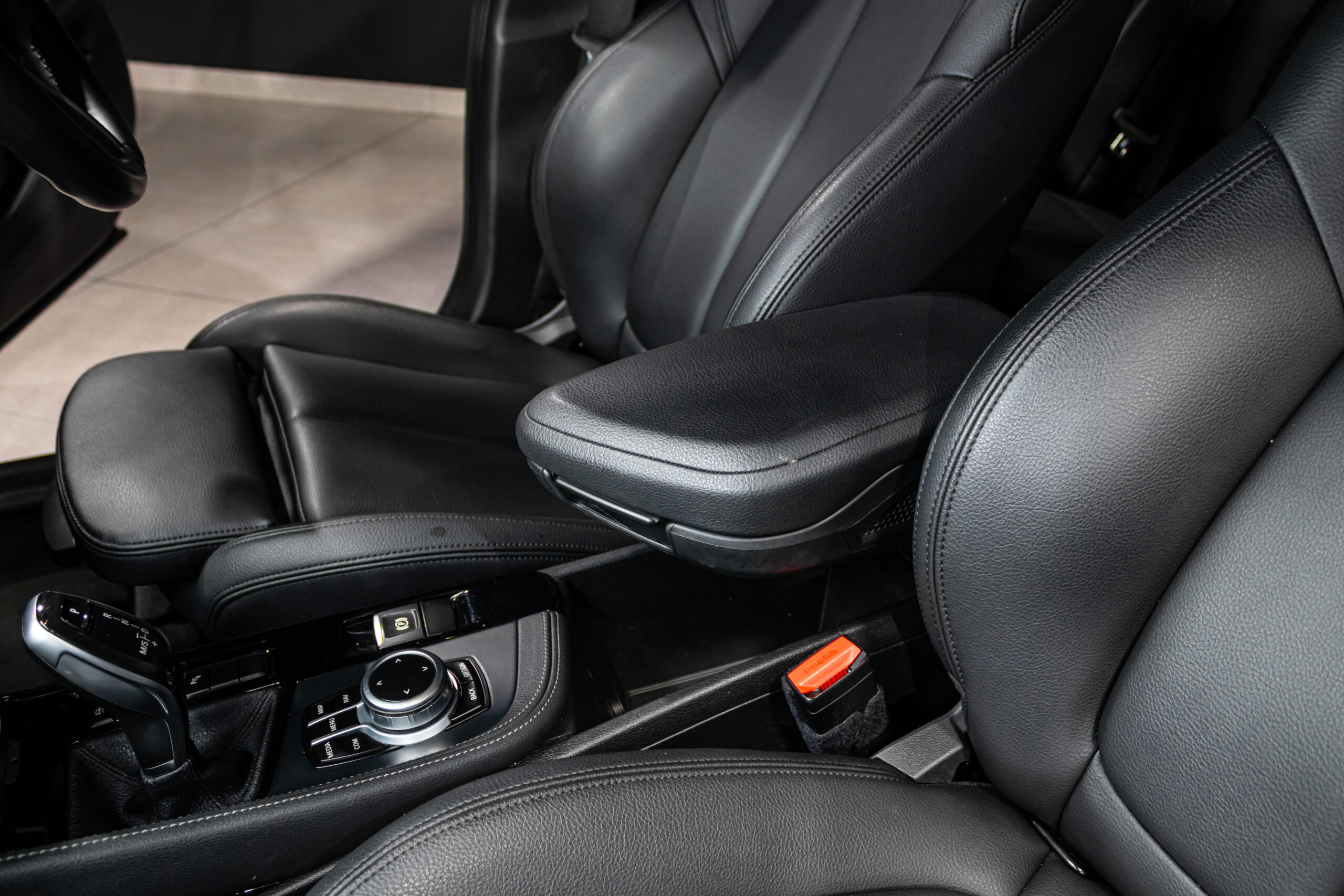 Black leather car interior with center console, armrest, and gear shifter viewed from the passenger side aisle area.