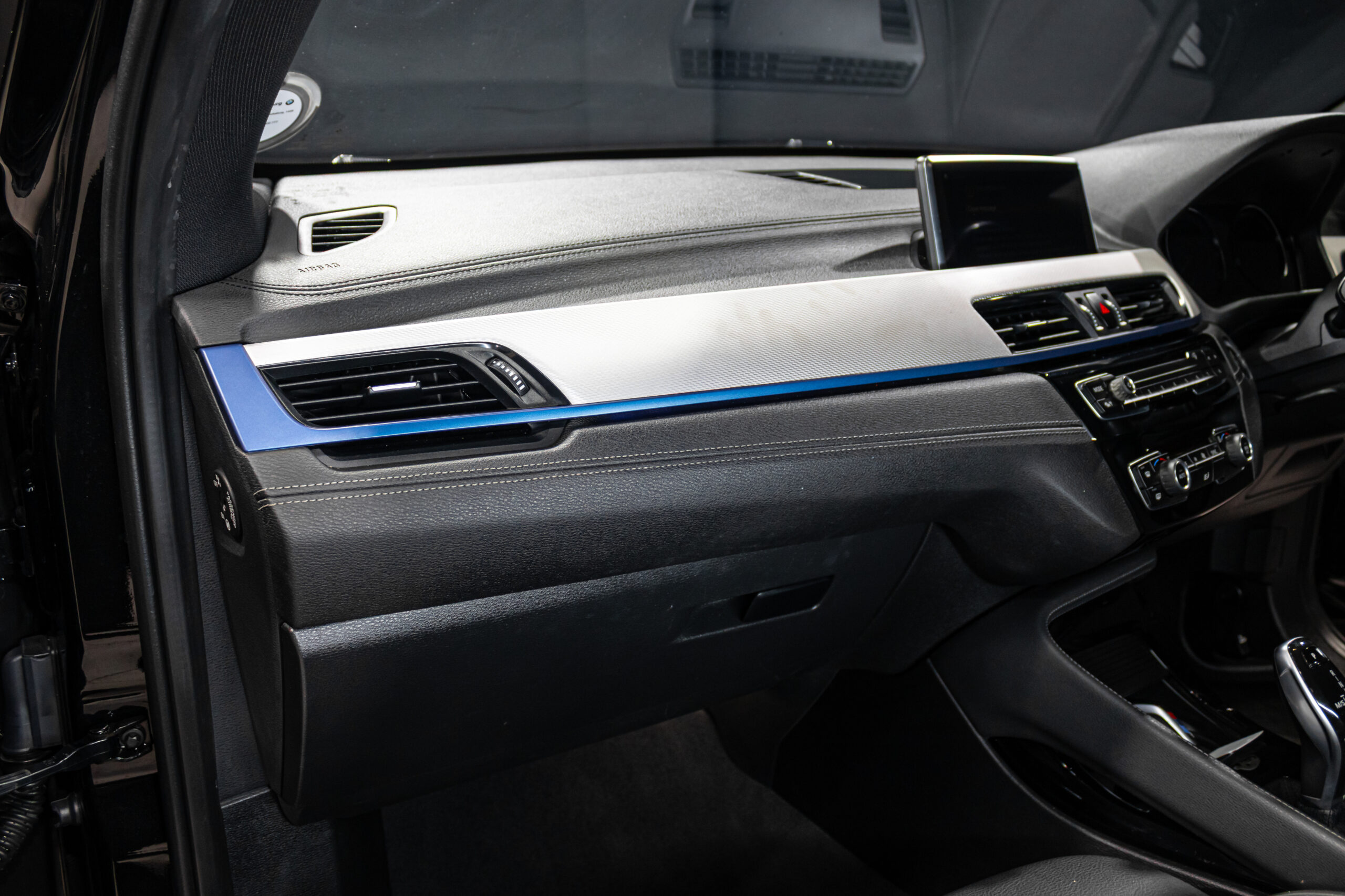Front passenger-side dashboard with silver trim, blue accent strip, air vents, and mounted display screen in a modern car int