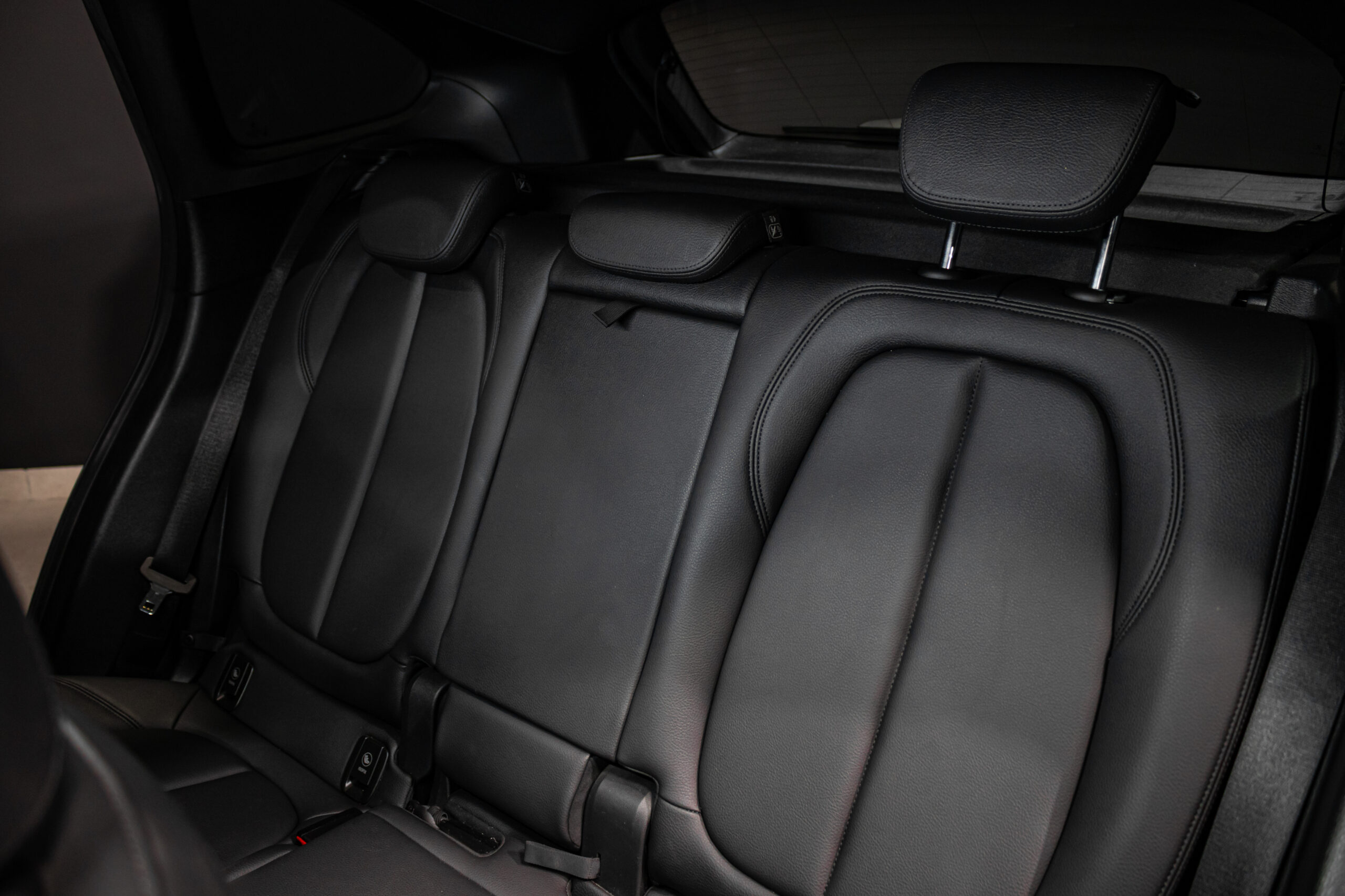 Black leather back seats of a car with three seating positions and headrests visible in the rear cabin.