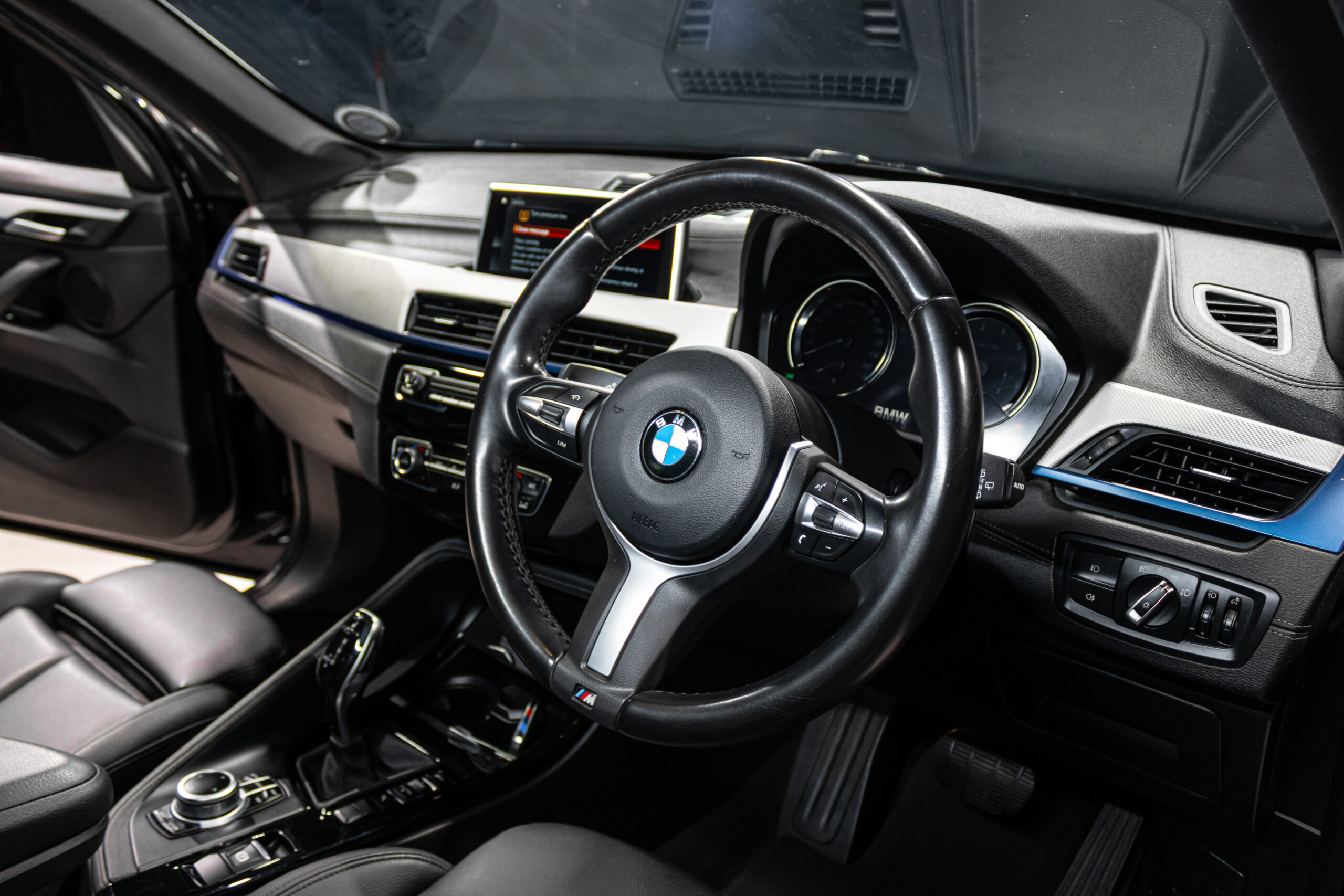 Close-up of a BMW car interior focusing on the black leather steering wheel with the BMW emblem and center console visible