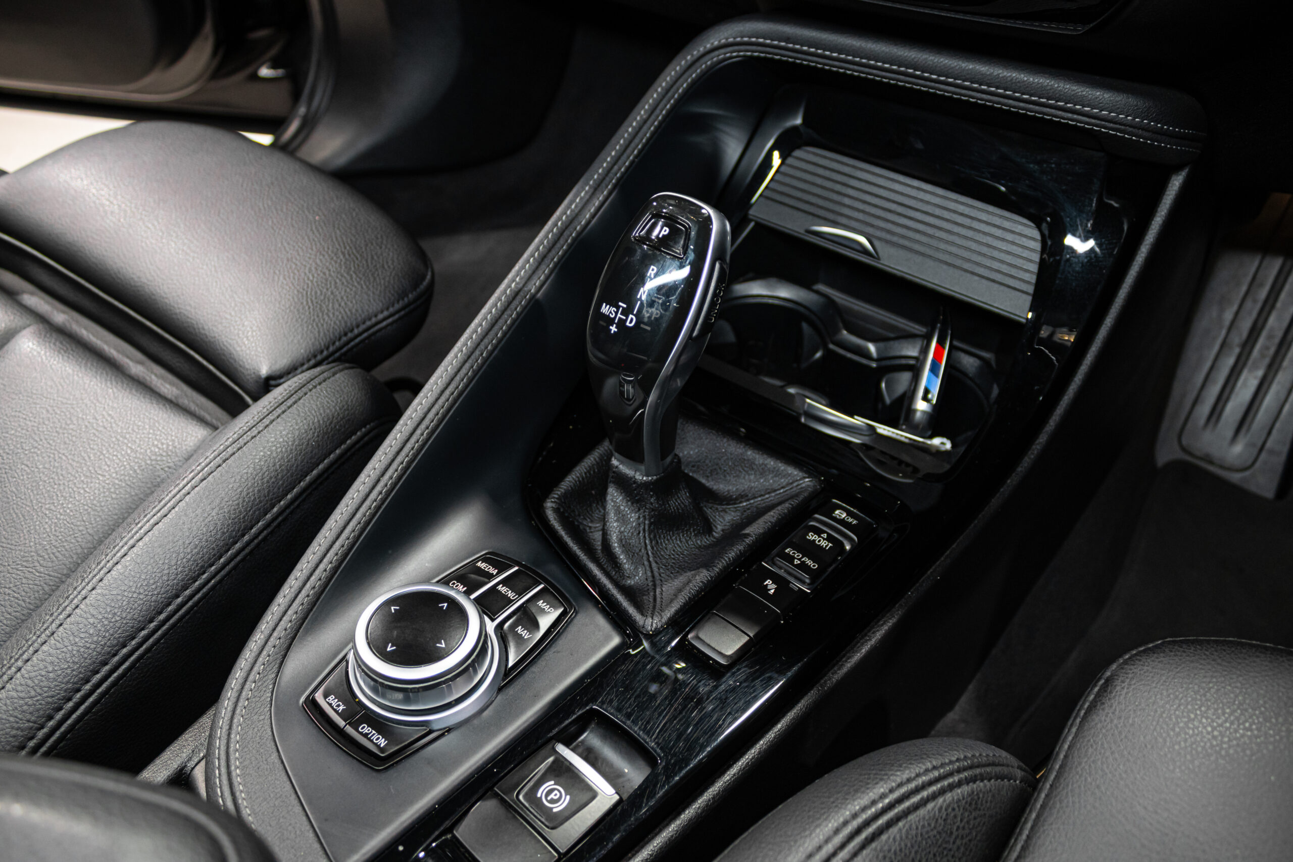 Center console of a car showing a gear shifter (P/R/N/D) and iDrive controller with surrounding buttons and cup holder area i