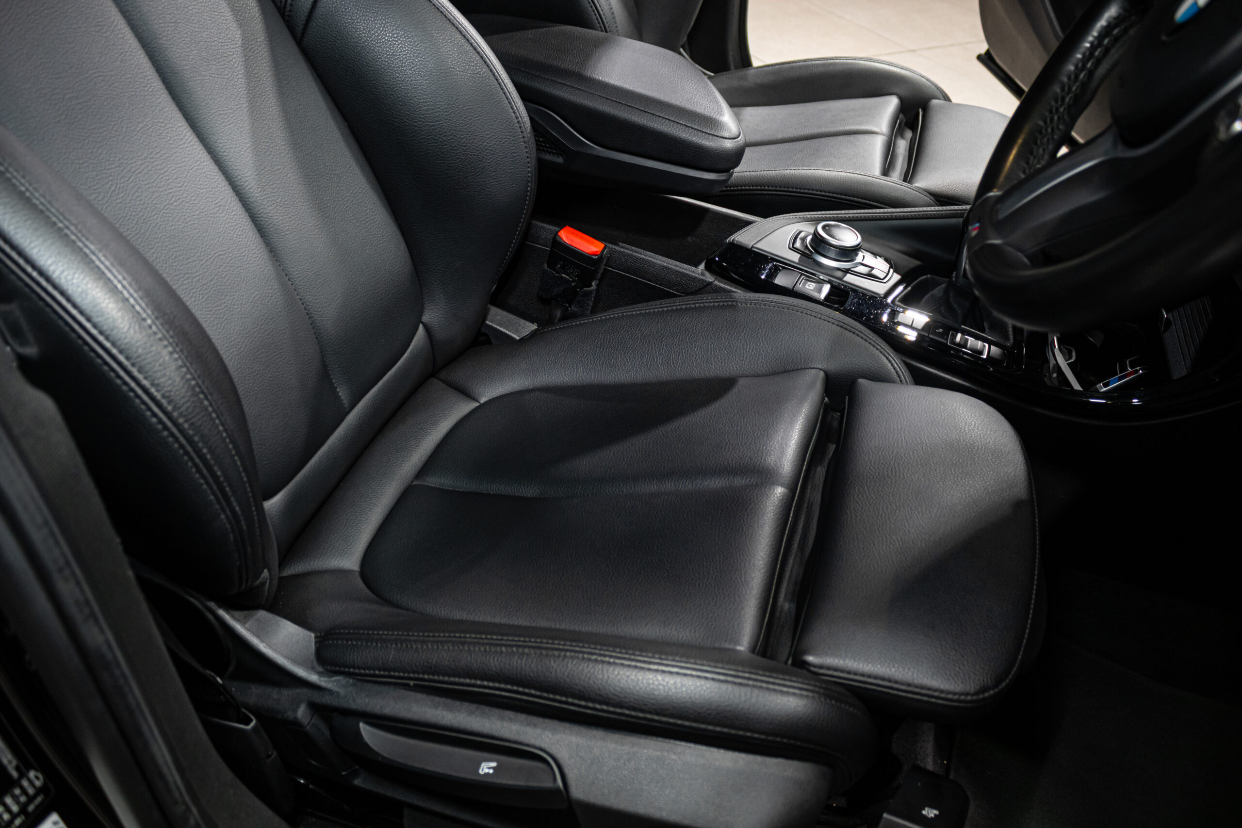 Black leather front seats and a glossy center console in a car, with a control dial and cupholder area visible.