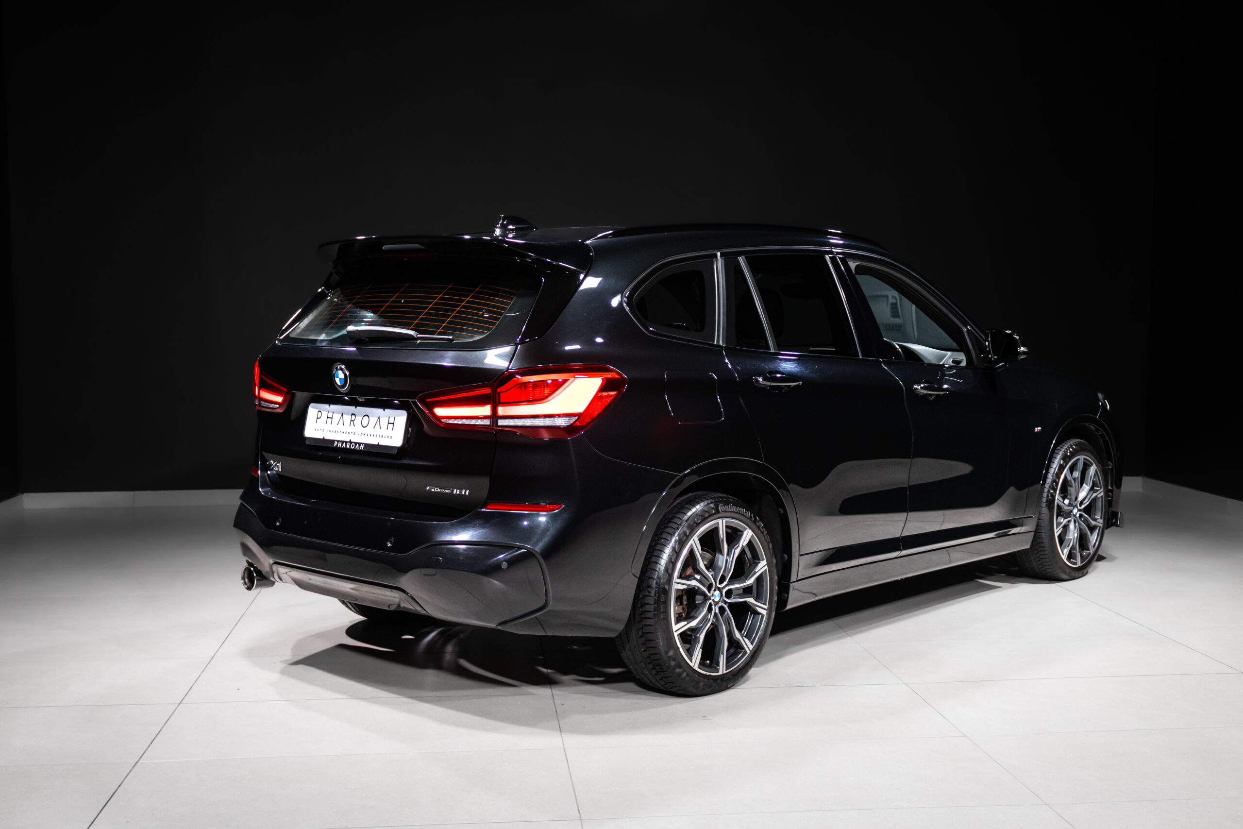 Rear three-quarter view of a black BMW SUV in a bright studio, showing red taillights and large alloy wheels.
