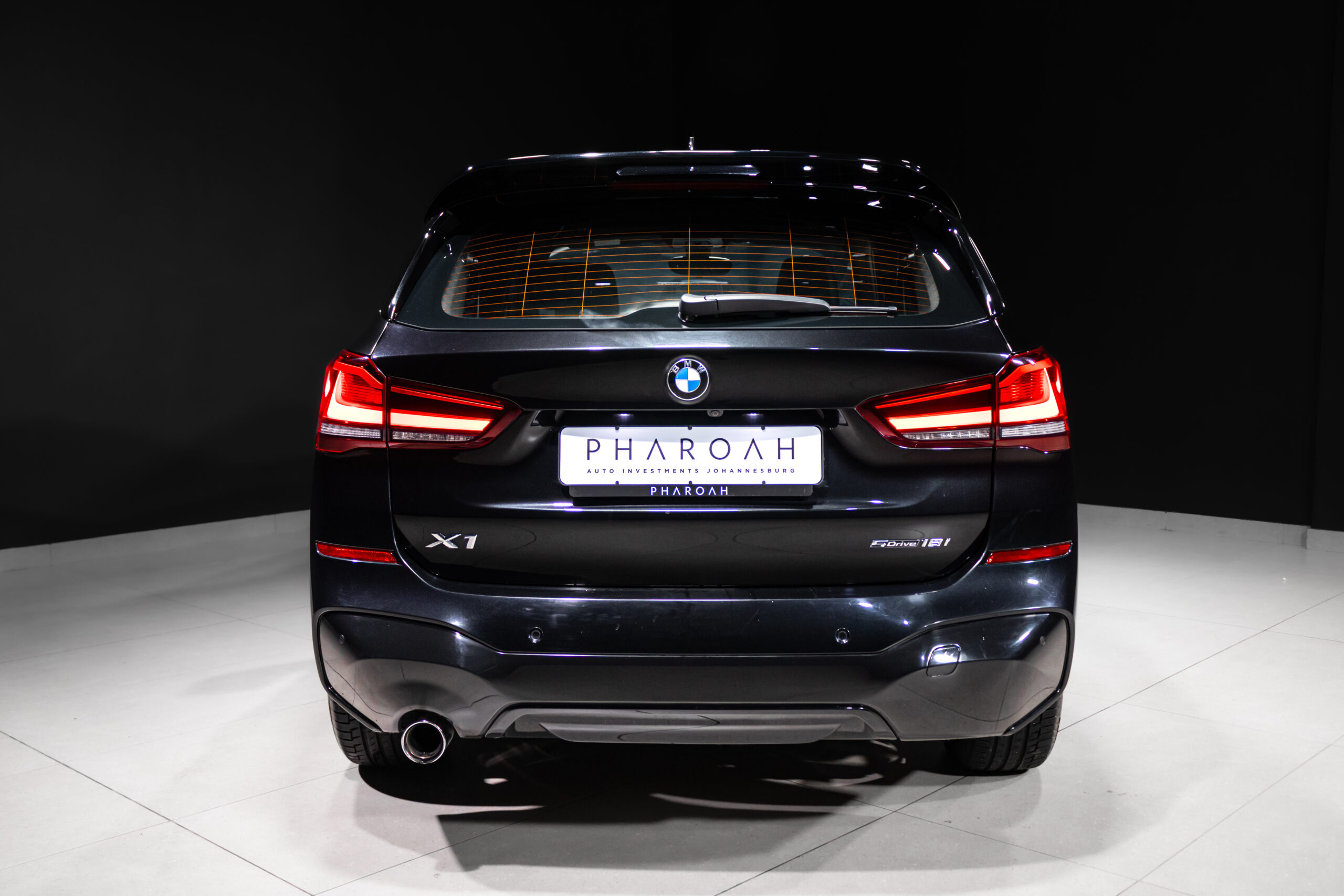 Rear view of a black BMW X1 in a studio, with bright red taillights and a PHAROH dealer plate.