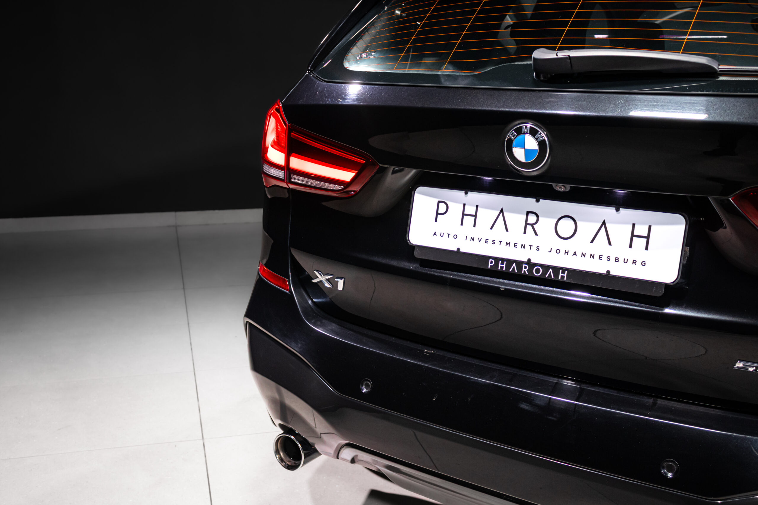 Rear view of a black BMW X1 showing the taillight, exhaust, and license plate that reads PHAROAH (Auto Investments Johannesbu